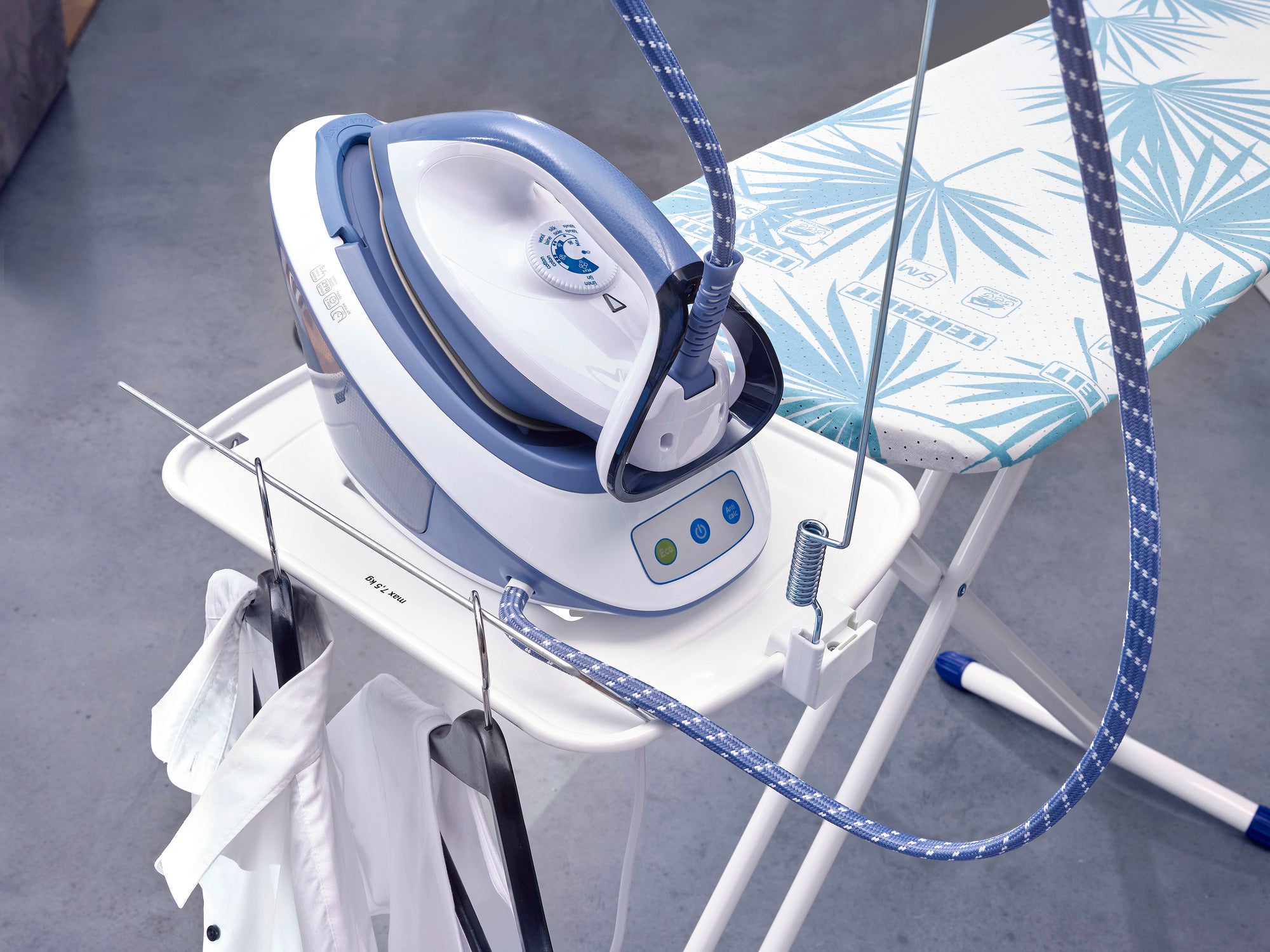 Bügeltisch Air Board Express M Solid mit Dampfbügeleisen. Der Tisch hat ein tropisches Muster und bietet Platz für hängende Kleidung. Ideal für effizientes Bügeln.