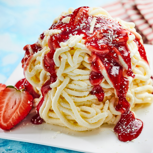 Ein Spaghetti-Eis mit Erdbeersosse und Puderzucker, garniert mit einer halben Erdbeere auf einem Teller.