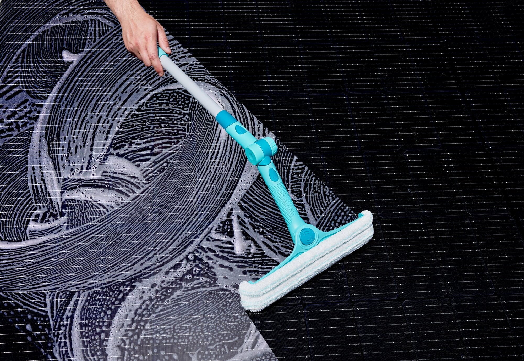 Ein Leifheit 4in1 FlexReach Fensterwischer reinigt eine große Glasfläche mit Seifenwasser. Der türkisfarbene Wischer hat einen ergonomischen Griff und flexible Gelenke.