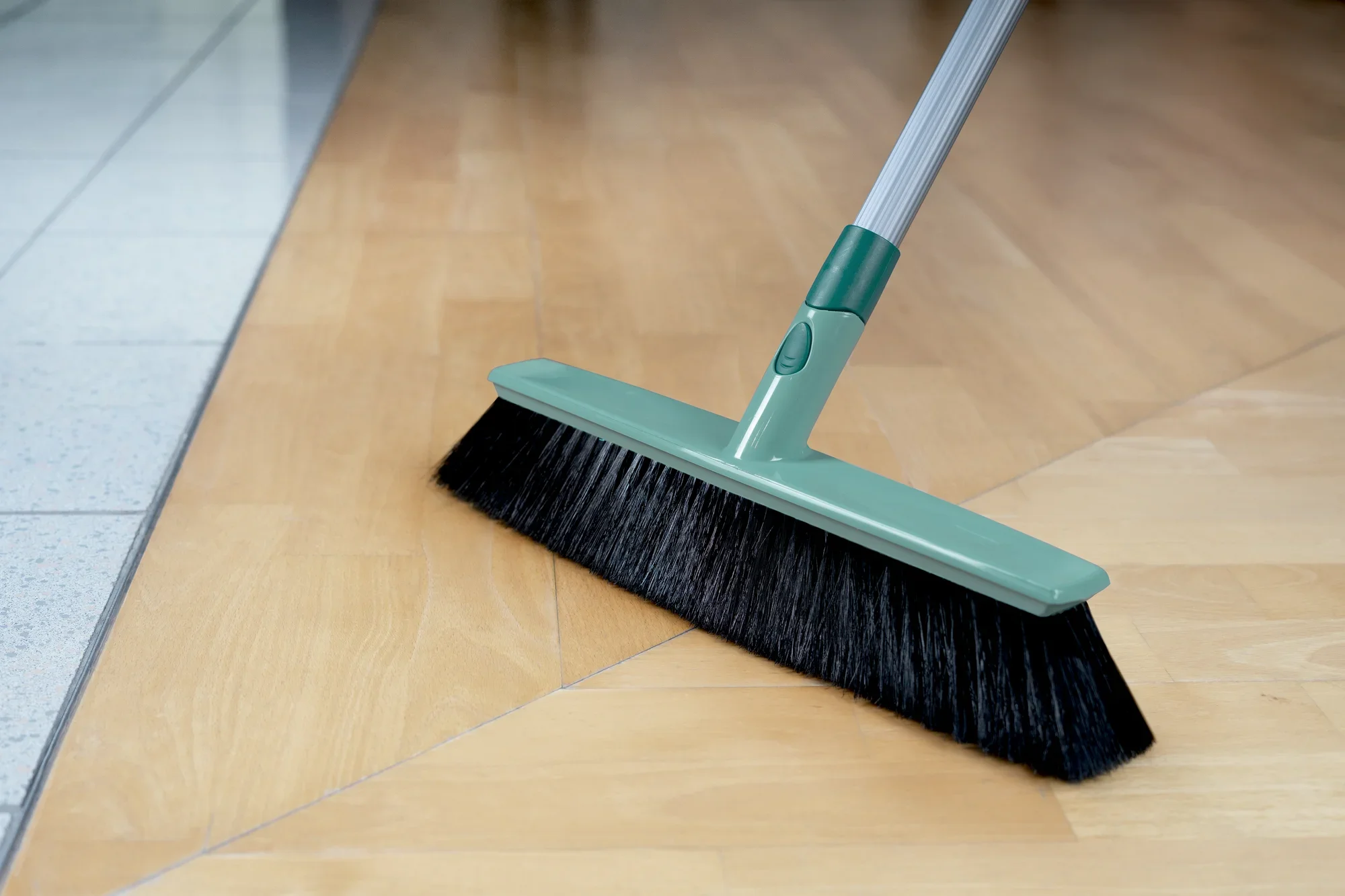 Ein Allround-Besen Xtra Clean mit einer Breite von 40 cm wird auf einem hellen Holzboden verwendet. Der Besen hat schwarze Borsten und einen grünen Griff, ideal für die gründliche Reinigung.