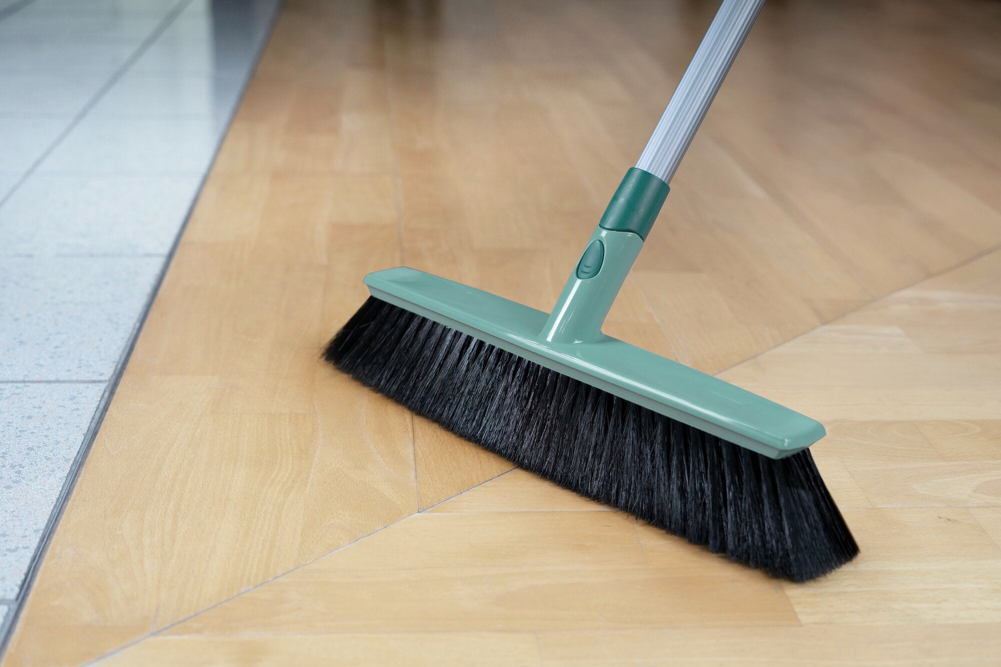 Una scopa multiuso Xtra Clean con una larghezza di 40 cm viene utilizzata su un pavimento in legno chiaro. La scopa ha setole nere e un manico verde, ideale per una pulizia accurata.