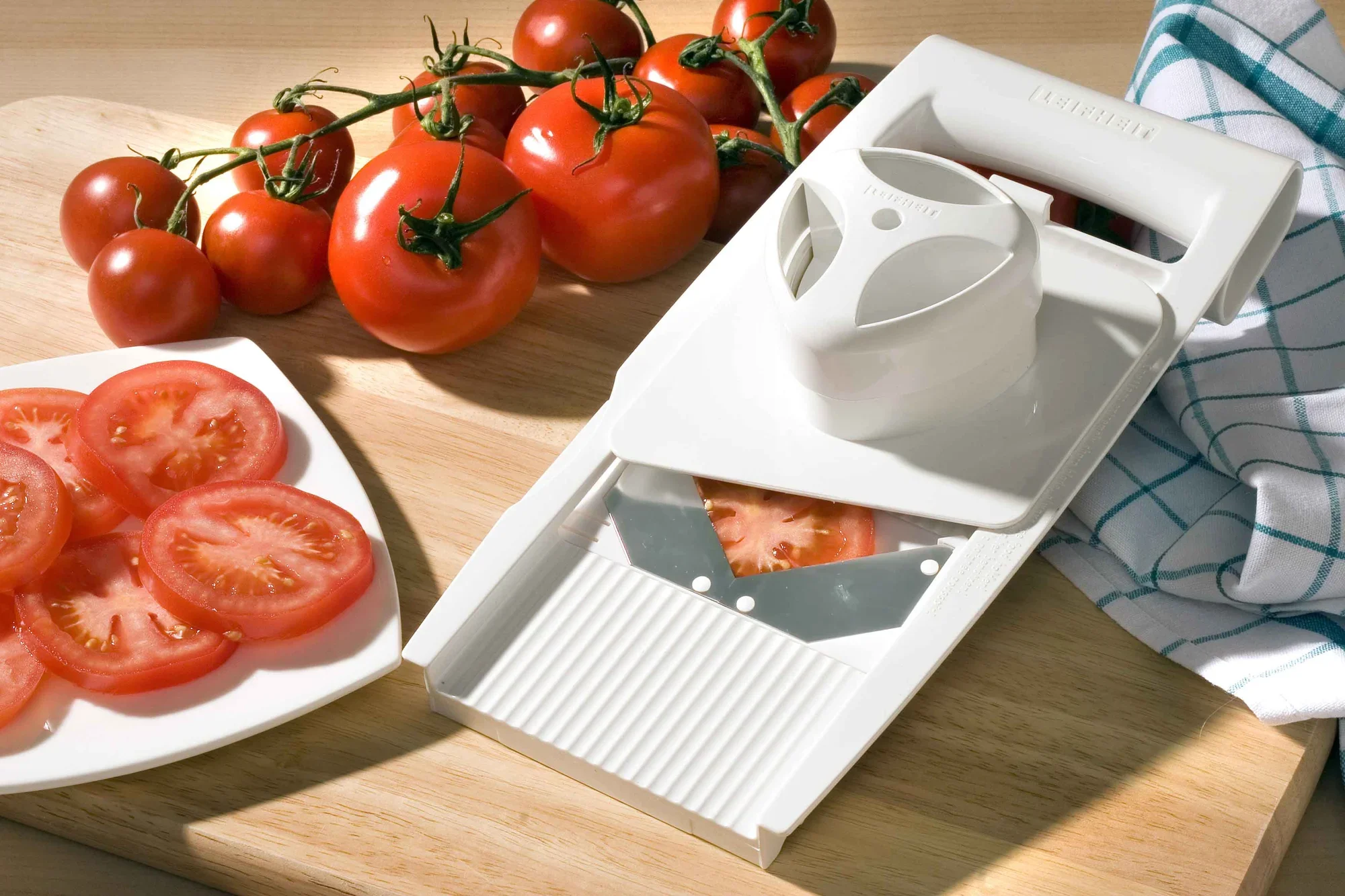 Universele rasp 4+1 op een houten tafel met verse tomaten. De rasp heeft een ergonomisch handvat en een scherp mes, ideaal voor het snijden van groenten.