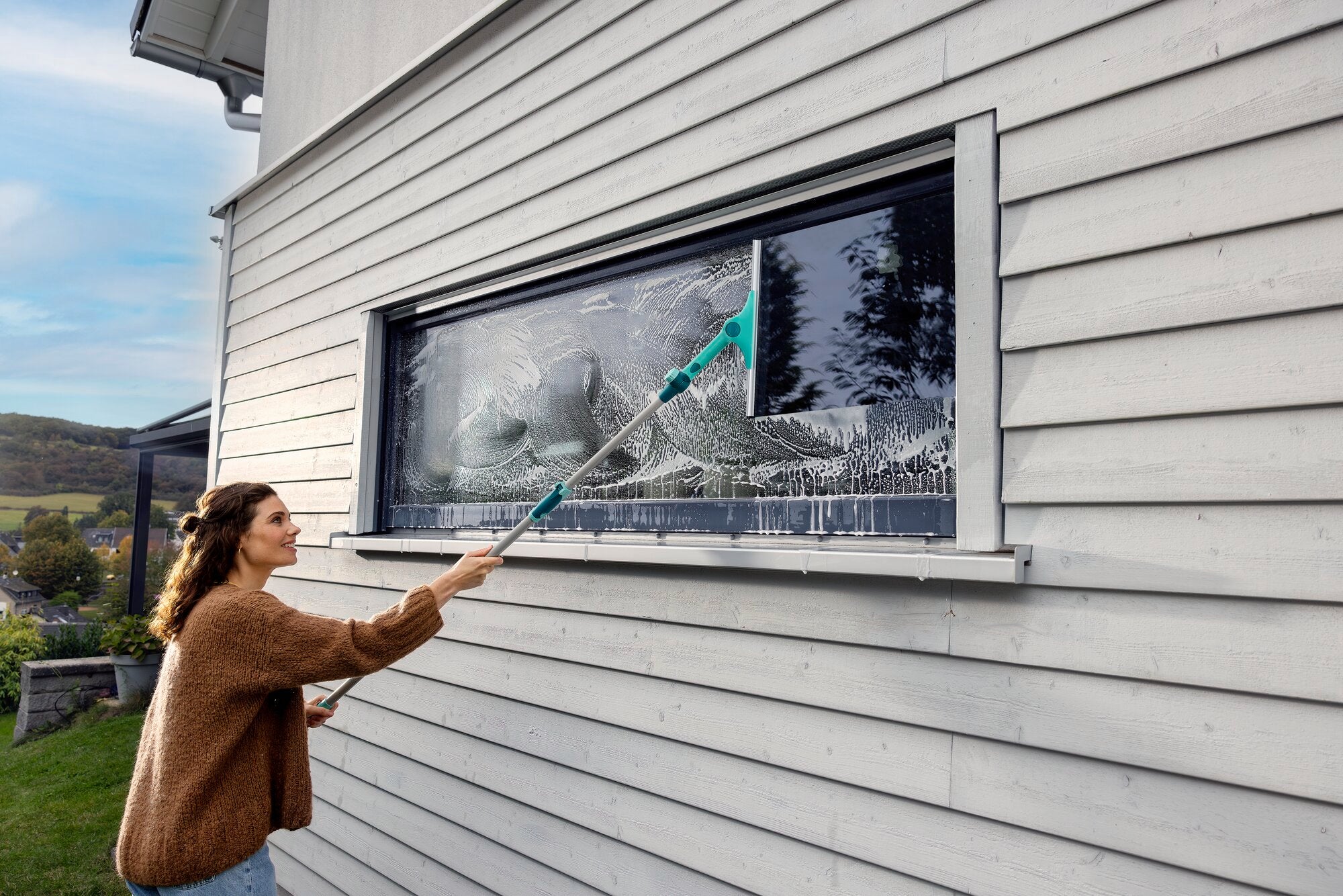Een vrouw maakt een groot raam schoon met de 2-in-1 XL ProReach telescopische raamreiniger. De reiniger heeft een lange steel, ideaal voor moeilijk bereikbare plaatsen.