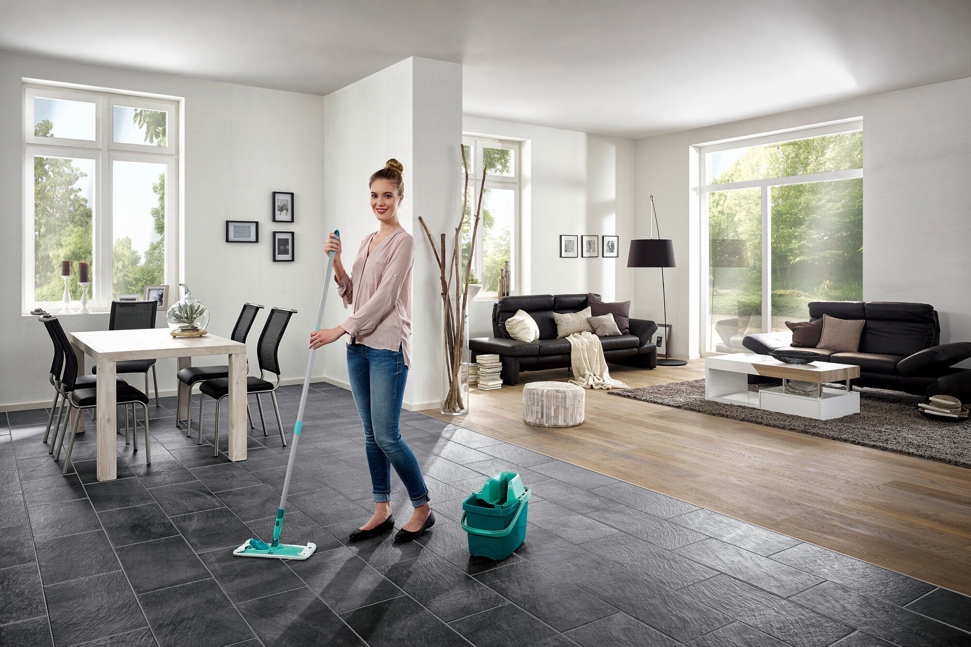 Eine Frau wischt den Boden eines modernen Wohnzimmers mit dem Bodenwischer Combi M. Der Raum ist hell und stilvoll eingerichtet, mit großen Fenstern und eleganten Möbeln.