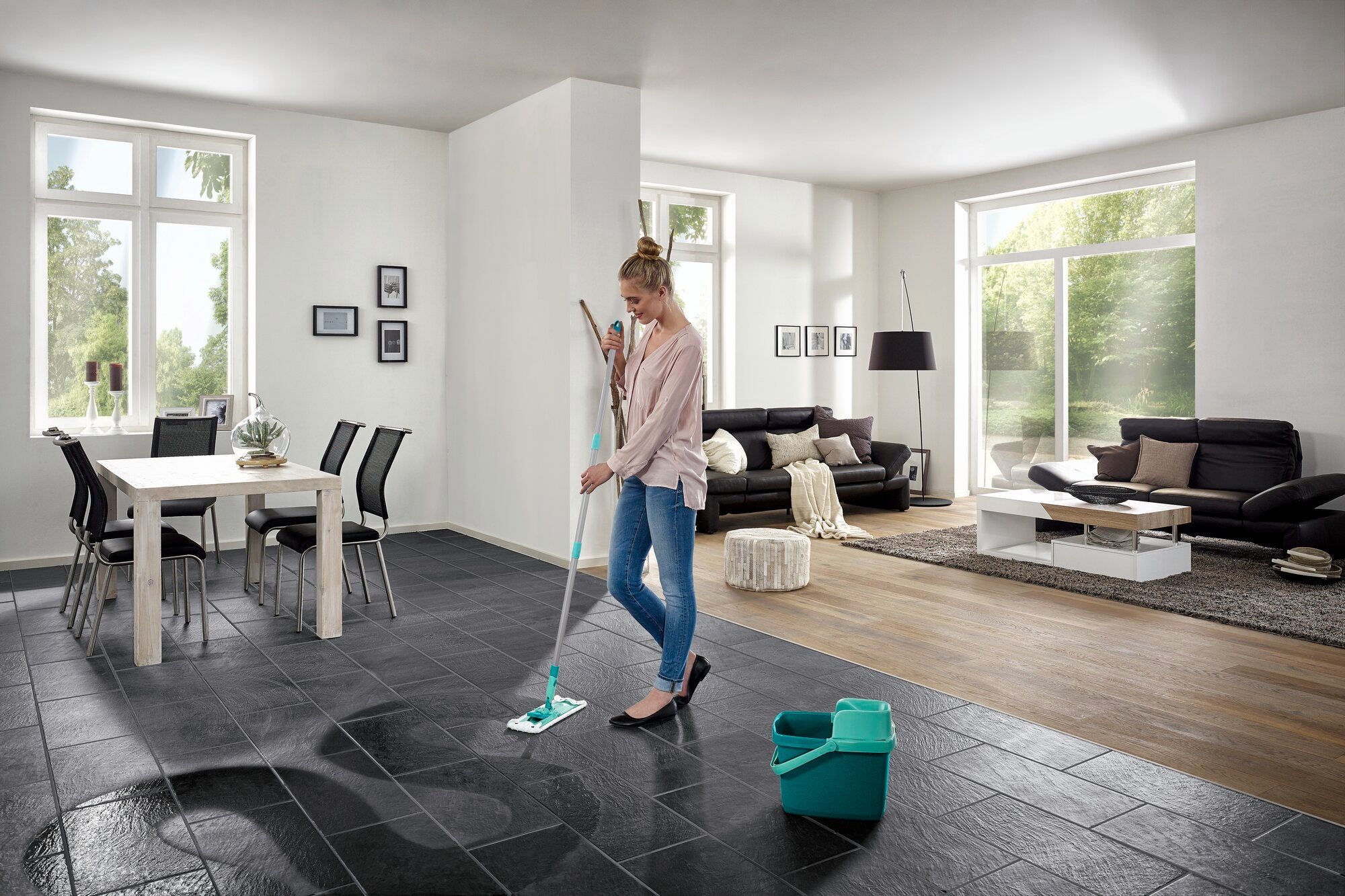 Eine Frau wischt den Boden in einem modernen Wohnzimmer mit dem Bodenwischer Combi M. Der Raum ist hell und stilvoll eingerichtet, mit großen Fenstern und eleganten Möbeln.