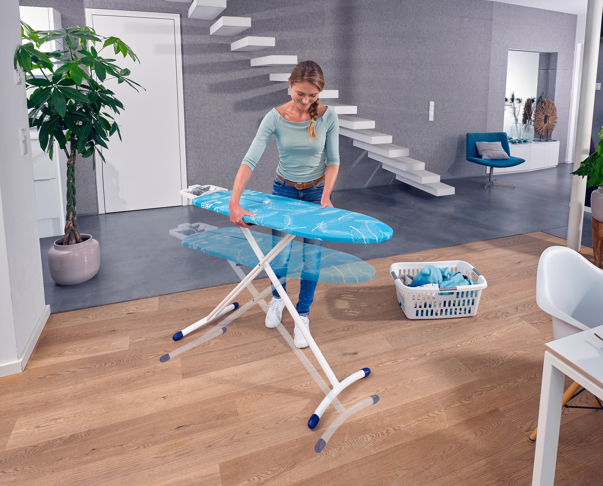 Eine Frau benutzt den Bügeltisch Air Board M Solid Plus in einem modernen Wohnzimmer. Der Tisch ist leicht und stabil, ideal für effizientes Bügeln.