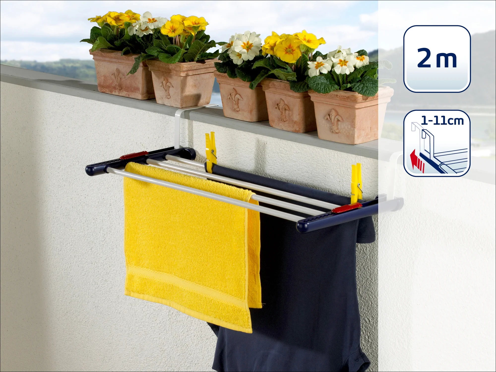 Een hangende droger is bevestigd aan een balkon waar twee handdoeken aan hangen. Op de achtergrond staan bloempotten met gele en witte bloemen. De droger is 2 meter lang en verstelbaar van 1 tot 11 cm.