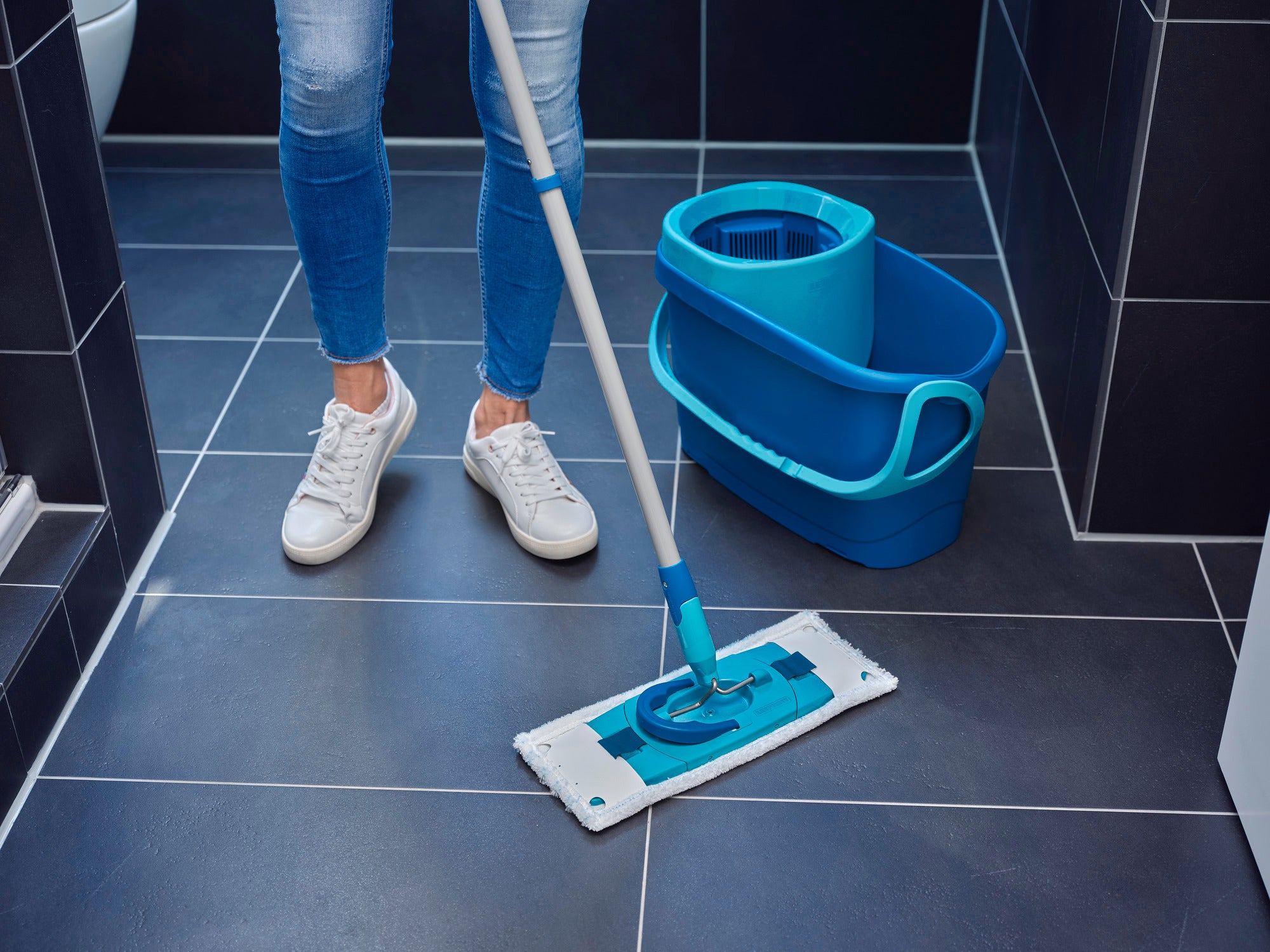 Eén persoon maakt een tegelvloer schoon met de CLEAN TWIST M micro duo vervangingsovertrek. De mop heeft een blauw design en wordt gebruikt met een bijpassende emmer. Ideaal voor een grondige schoonmaakbeurt.