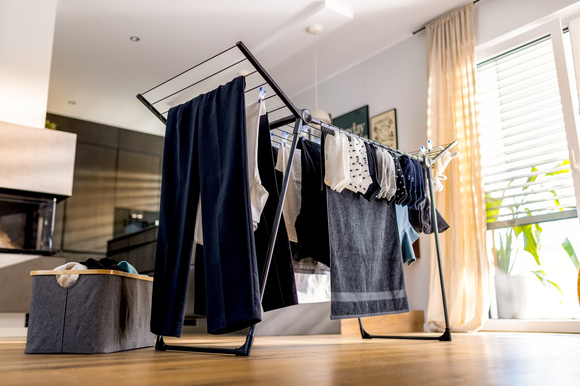 Leifheit Standtrockner Pegasus Slim 15 m Black in modernem Wohnraum mit aufgeklappten Flügeln, behängt mit Hosen, Handtüchern und Wäsche; schlankes schwarzes Design auf hellem Holzboden.