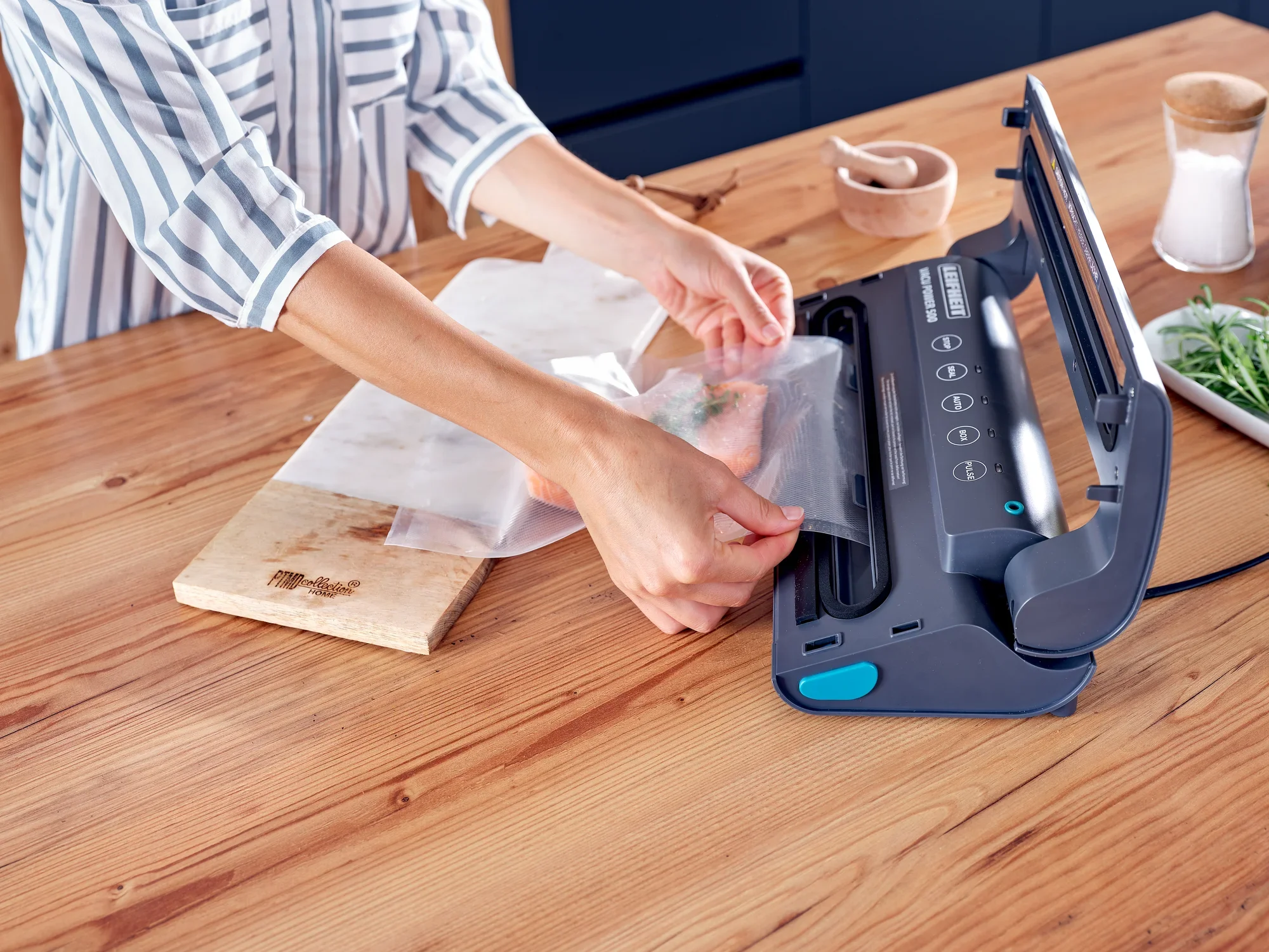 Osoba używa zgrzewarki próżniowej Vacu Power 500 do zamykania żywności w torebce. Urządzenie stoi na drewnianym stole w nowoczesnej kuchni.