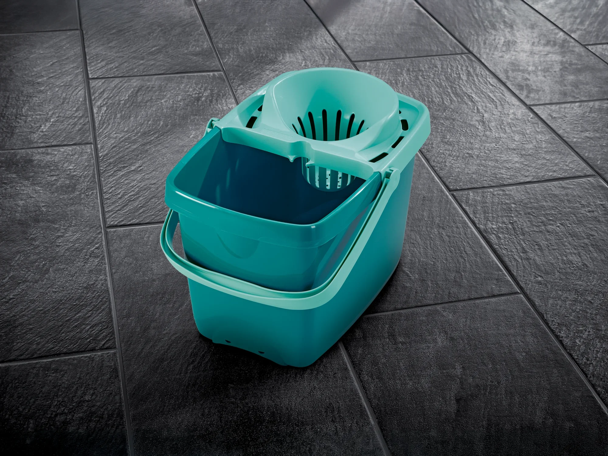 Een turkoois gekleurde Profi XL emmer met geïntegreerde zeef staat op een donkere tegelvloer. De emmer is robuust en ideaal voor een efficiënte vloerreiniging.