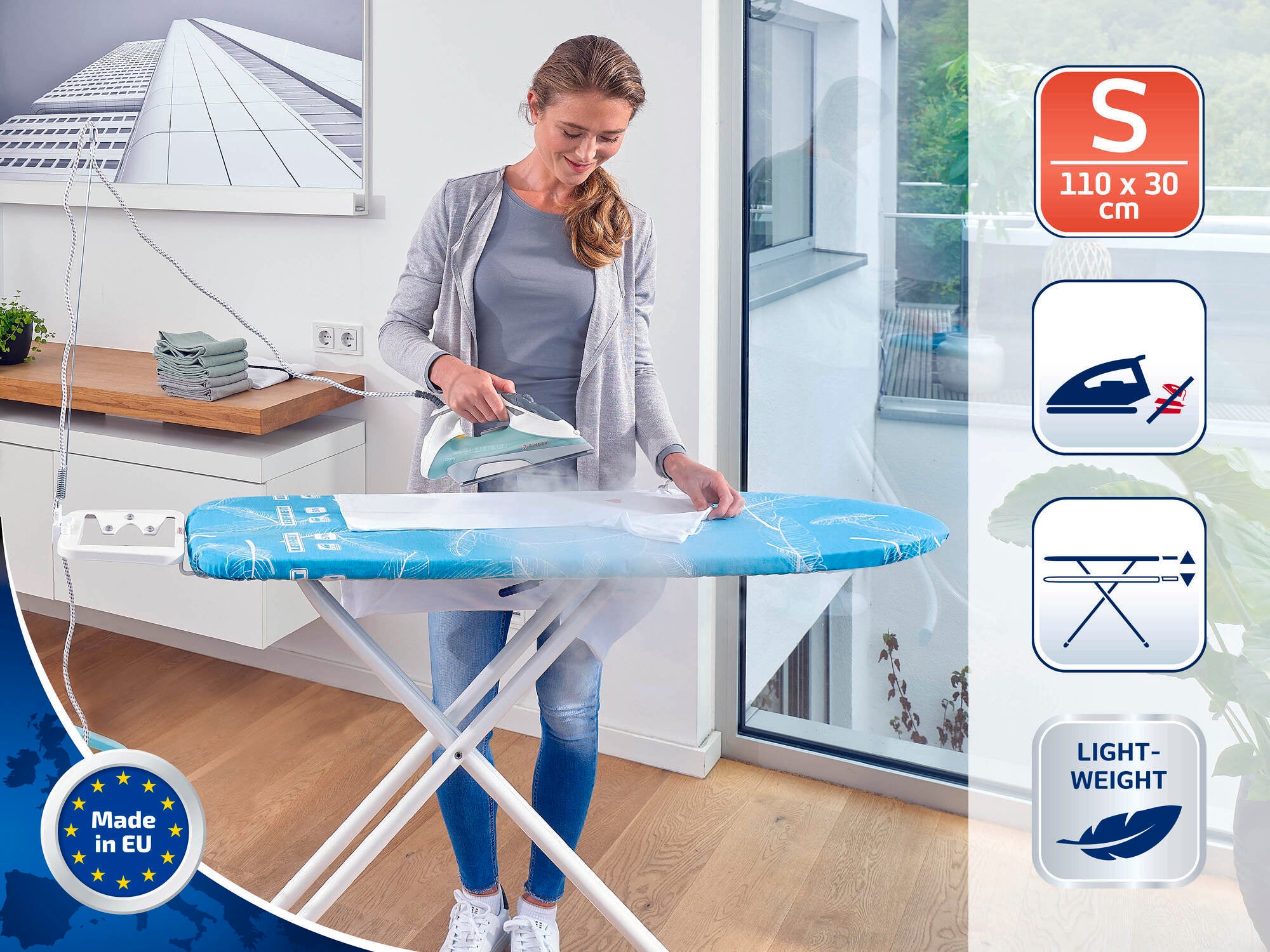 Une femme repasse sur une table à repasser bleue dans une pièce moderne. La table est légère et compacte (110 x 30 cm), idéale pour les petites pièces. Fabriquée dans l'UE.