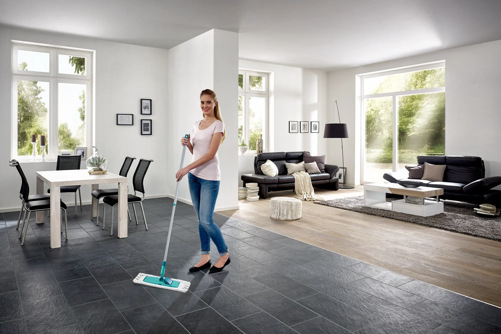 Een vrouw dweilt de vloer in een moderne woonkamer met de Profi XL dweilmop. De kamer is licht en stijlvol ingericht, met grote ramen en elegante meubels.