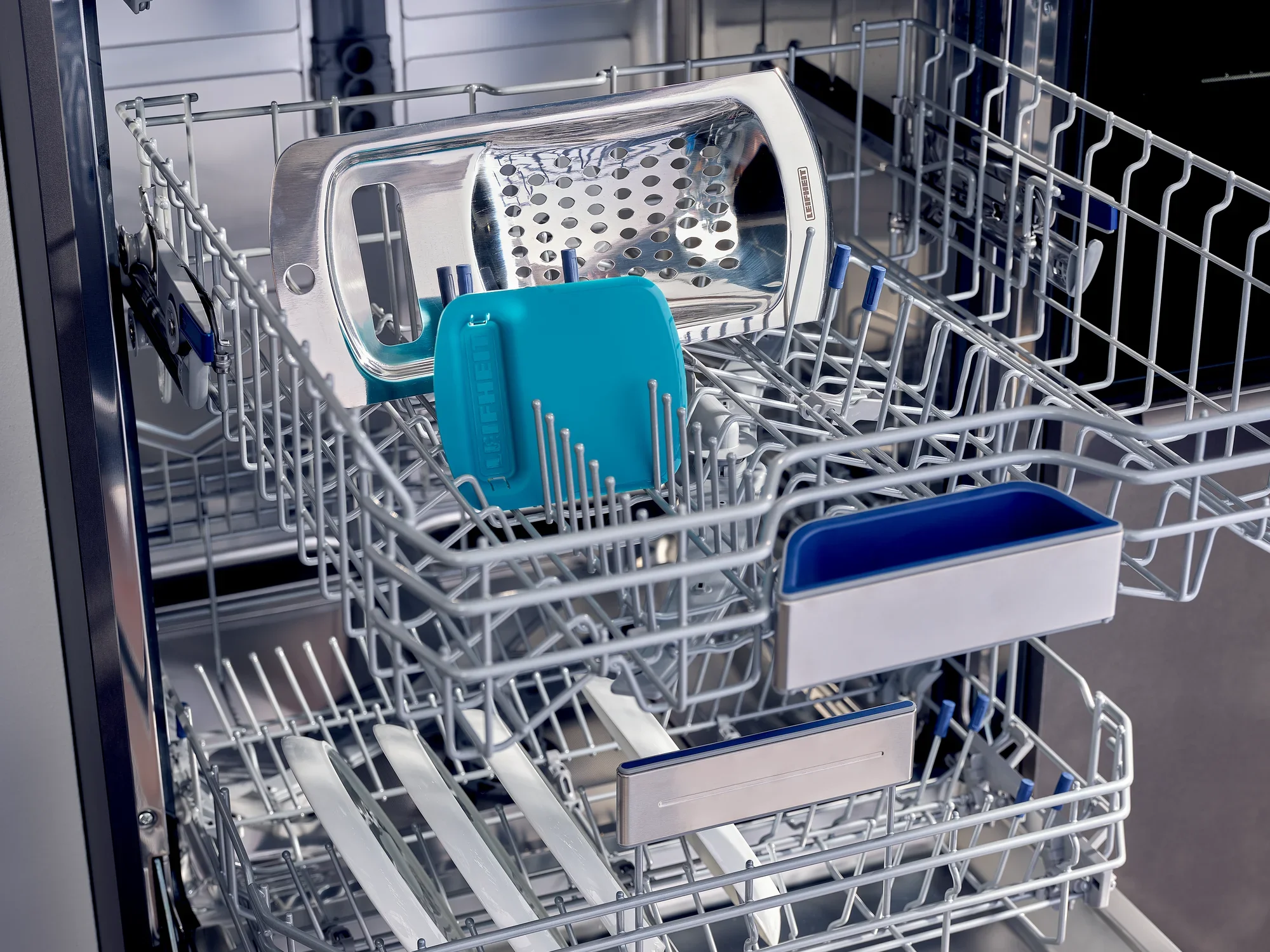 Râpe à spätzle et râpe dans un lave-vaisselle. La râpe à spätzle est turquoise et se trouve à côté d'une râpe argentée dans le compartiment supérieur du lave-vaisselle.