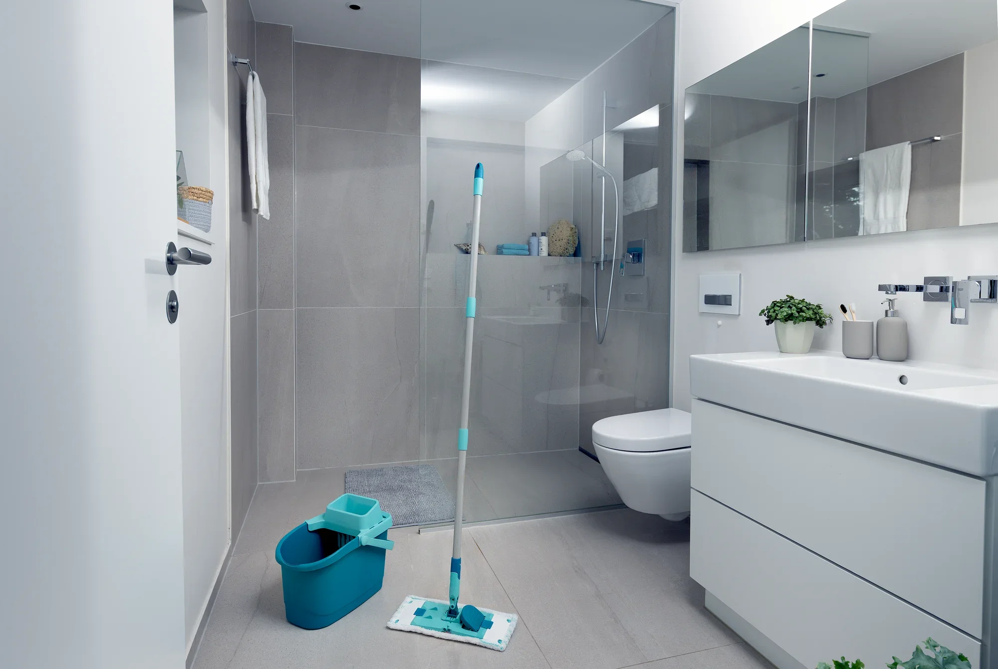 Une salle de bain moderne équipée d'un kit POWER CLEAN. Le balai à franges est posé à côté d'un seau sur le carrelage clair. L'environnement semble propre et rangé, idéal pour un nettoyage en profondeur.