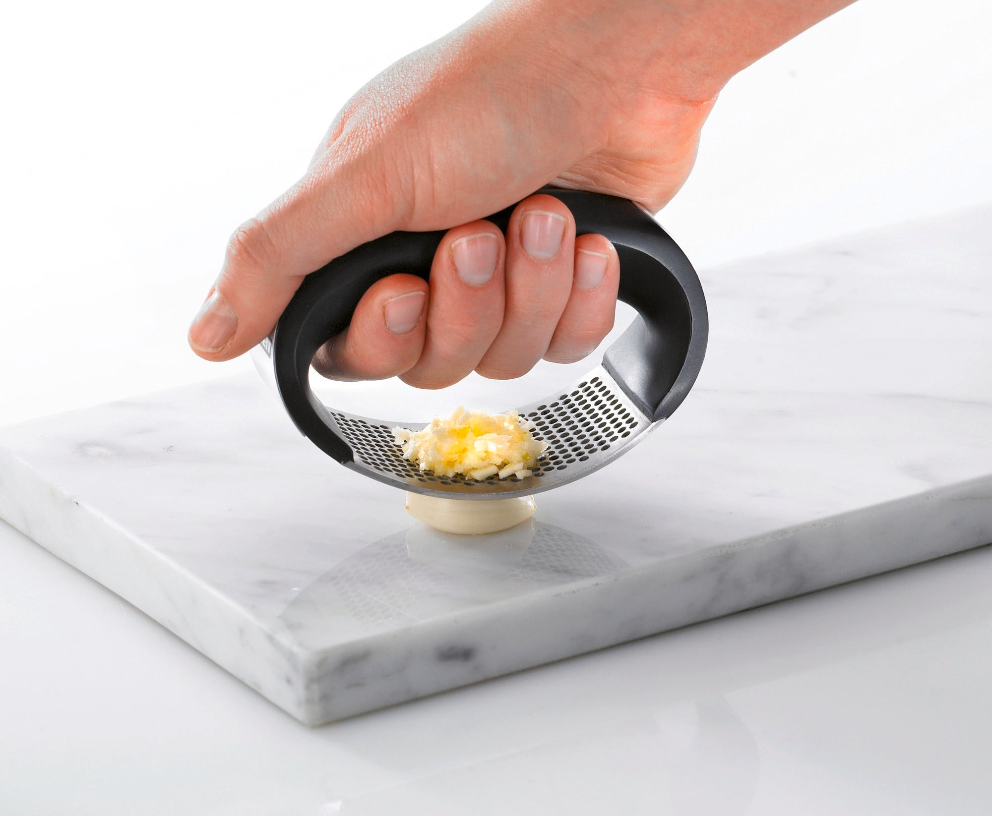 Knobi-King Knoblauchpresse in Aktion: Eine Hand drückt die ergonomische Presse auf eine Knoblauchzehe, um sie auf einem Marmorbrett zu zerkleinern. Ideal für die Küche.