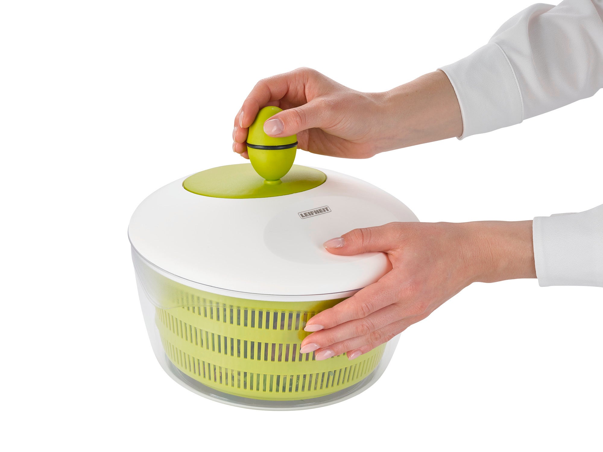 Trend salad spinner, 4.2 l, in use. Two hands operate the green knob on the white lid of the transparent bowl to dry salad efficiently.
