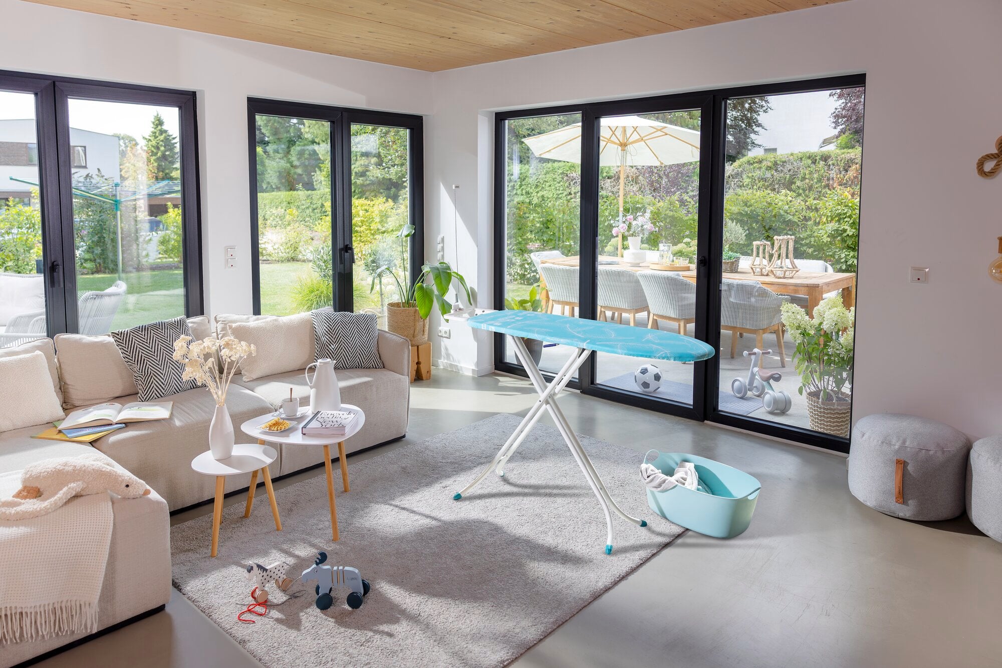 Bügelbrett Leifheit Air Board M Compact in einem modernen Wohnzimmer mit großen Fenstern. Das Brett steht auf einem Teppich, umgeben von gemütlichen Möbeln und Pflanzen.