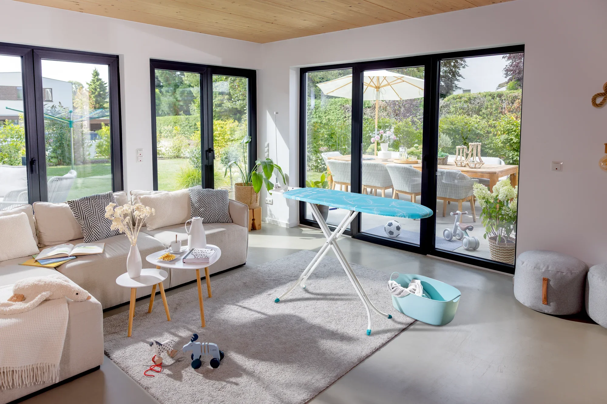 Bügelbrett Leifheit Air Board M Compact in einem modernen Wohnzimmer mit großen Fenstern. Das Brett steht auf einem Teppich, umgeben von gemütlichen Möbeln und Pflanzen.