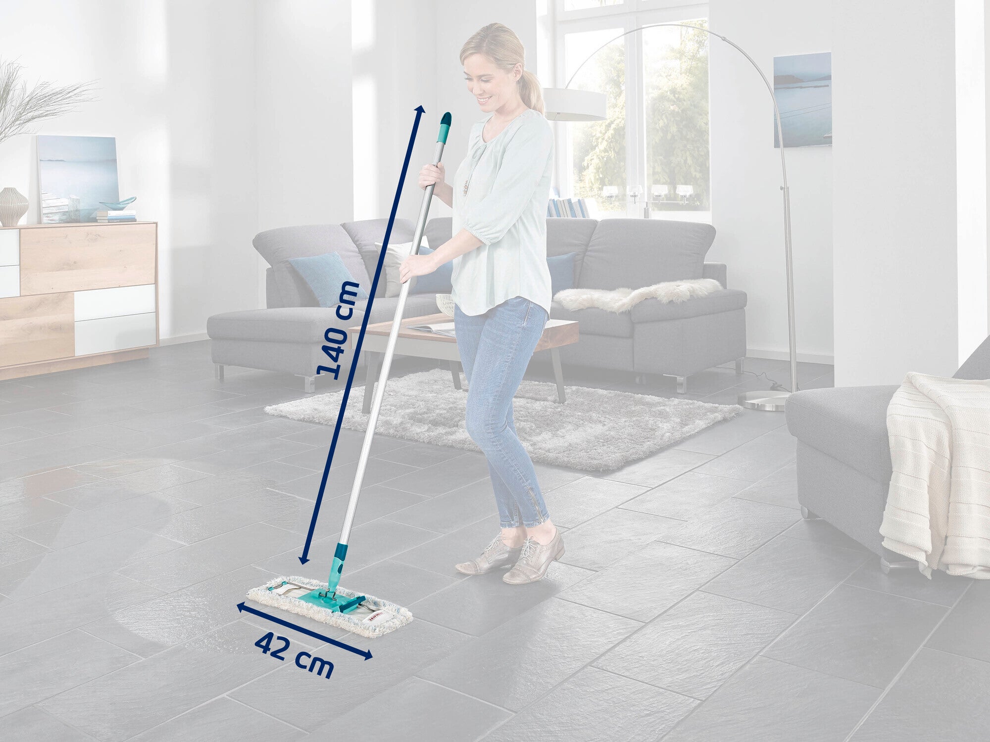 Eine Frau reinigt den Boden eines modernen Wohnzimmers mit einem Bodenwischer. Der Bodenwischer hat eine Länge von 140 cm und eine Breite von 42 cm. Im Hintergrund sind ein Sofa und ein Teppich zu sehen.