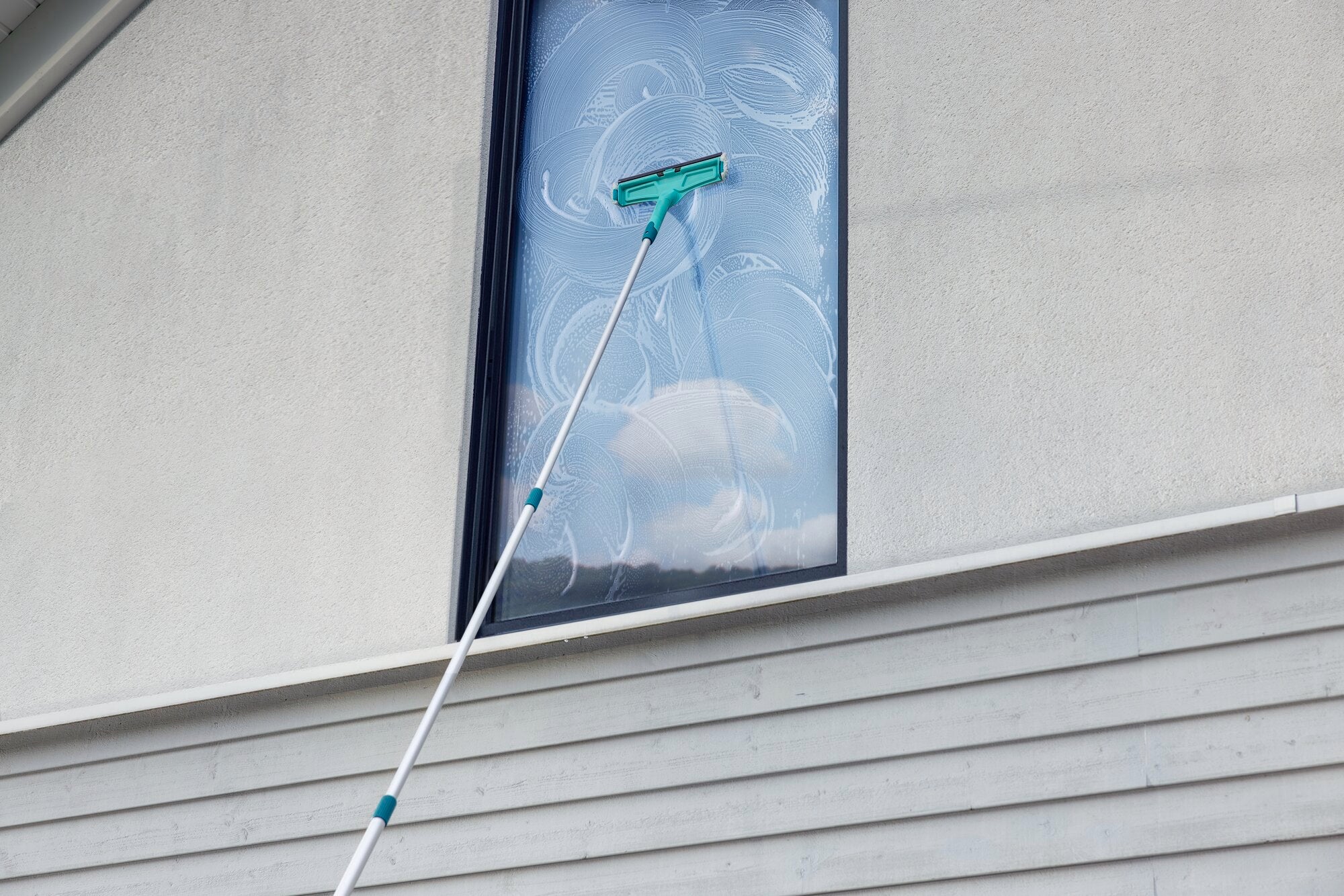 Teleskopstiel 145 bis 400 cm: Ein Teleskopstiel wird verwendet, um ein hohes Fenster zu reinigen. Der Stiel ist ausgefahren, um schwer erreichbare Stellen zu säubern.