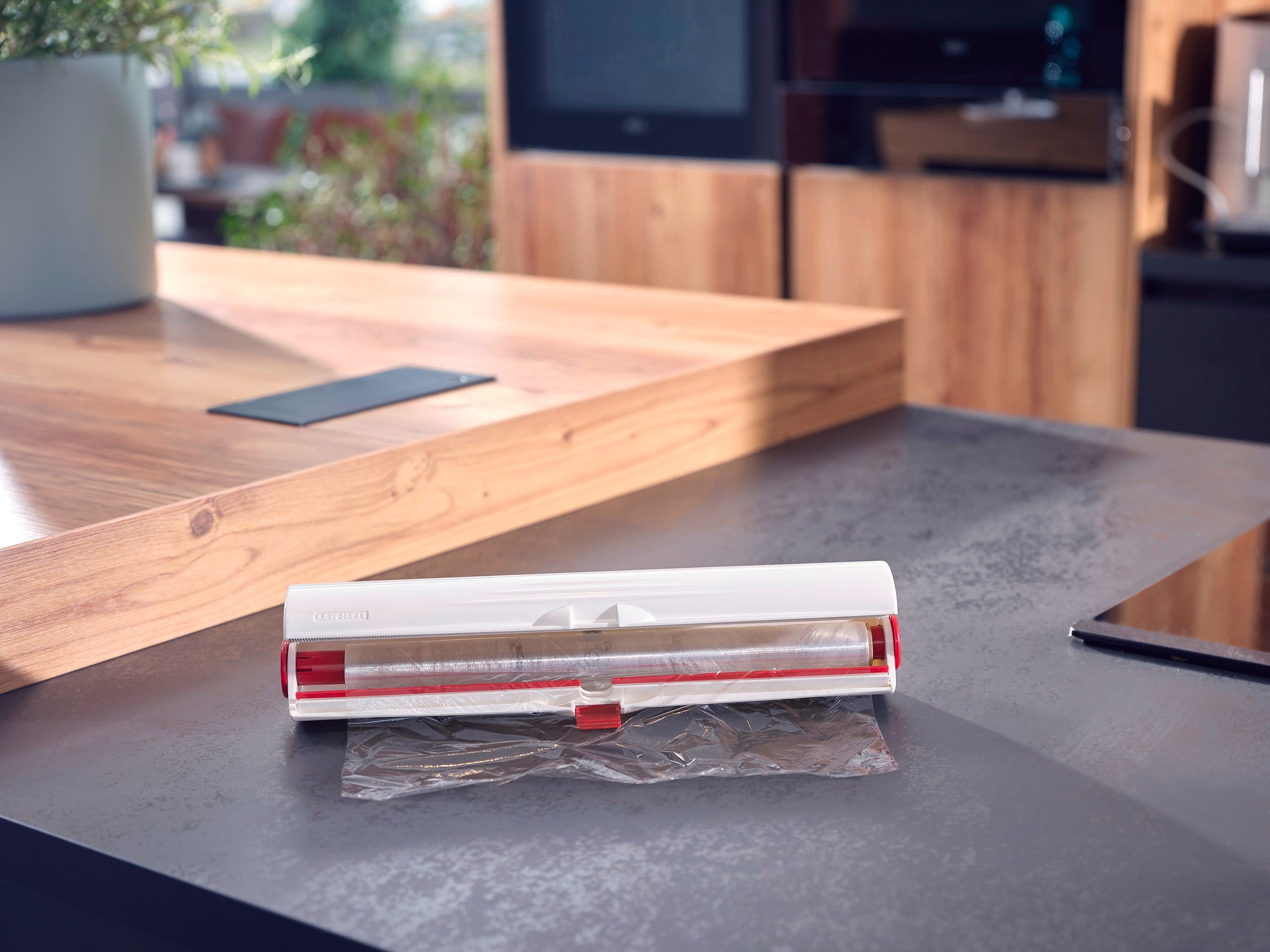 Cutter pour film Perfect Cut sur un plan de travail moderne. L'appareil est blanc avec des accents rouges et coupe avec précision le film alimentaire. Idéal pour une cuisine élégante.