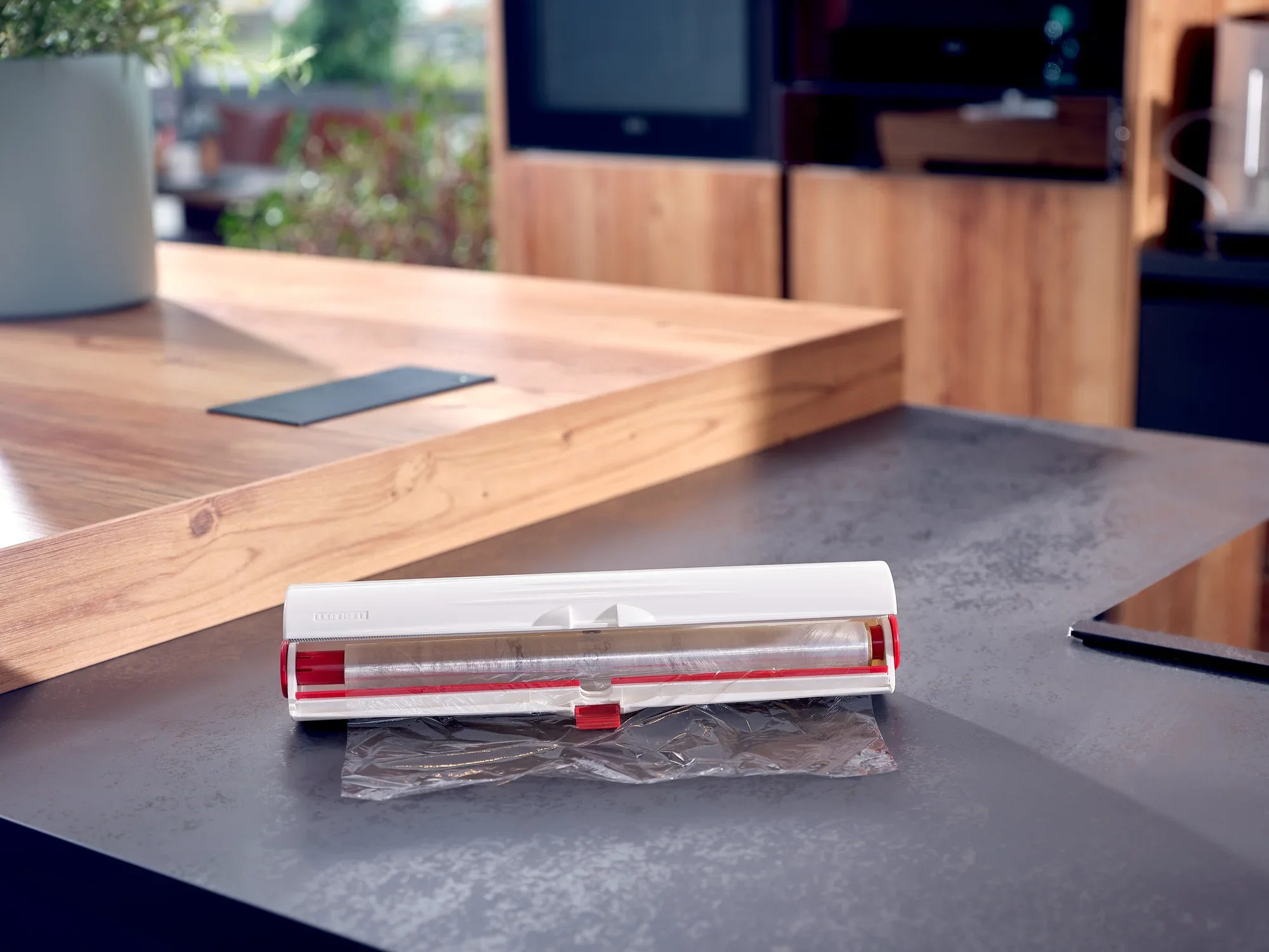 Perfect Cut foil cutter on a modern kitchen worktop. The device is white with red accents and cuts cling film precisely. Ideal for a stylish kitchen.