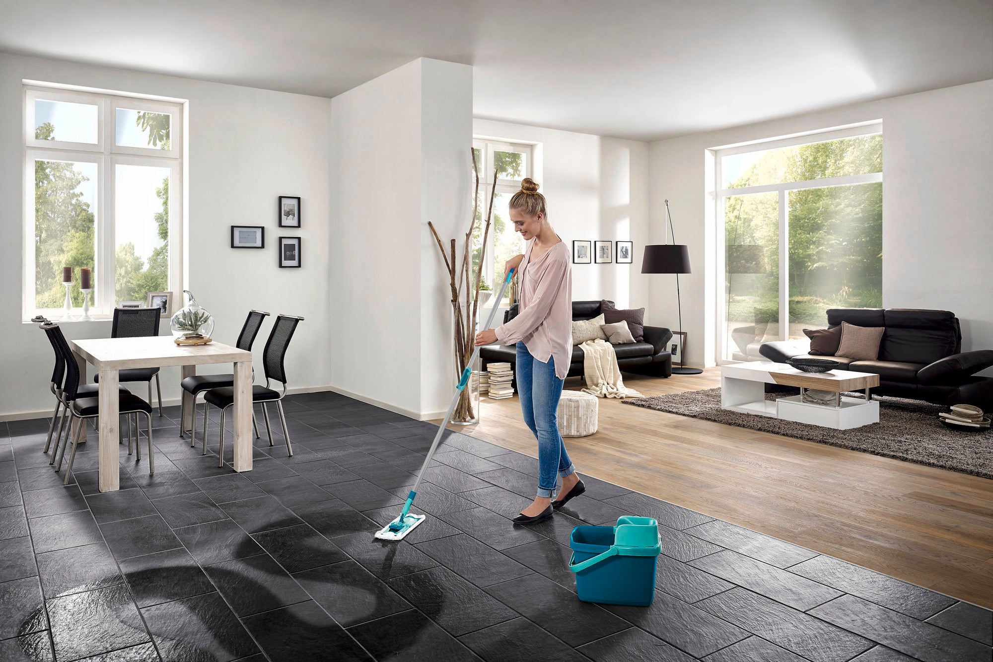 Eine Frau wischt den Boden in einem modernen Wohnzimmer mit dem Bodenwischer Combi M micro duo. Der Raum ist hell und stilvoll eingerichtet, mit großen Fenstern und eleganten Möbeln.