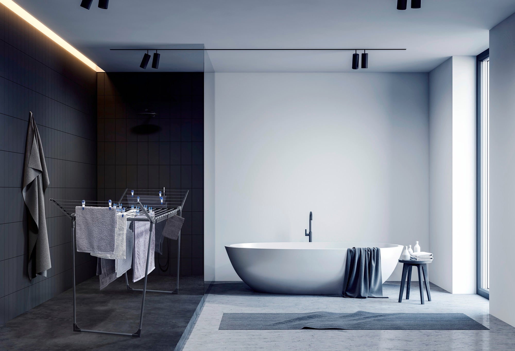 Standtrockner Pegasus 180 Solid in einem modernen Badezimmer mit dunklen Fliesen und einer freistehenden Badewanne. Der Trockner ist mit Handtüchern beladen und steht neben der Wanne.