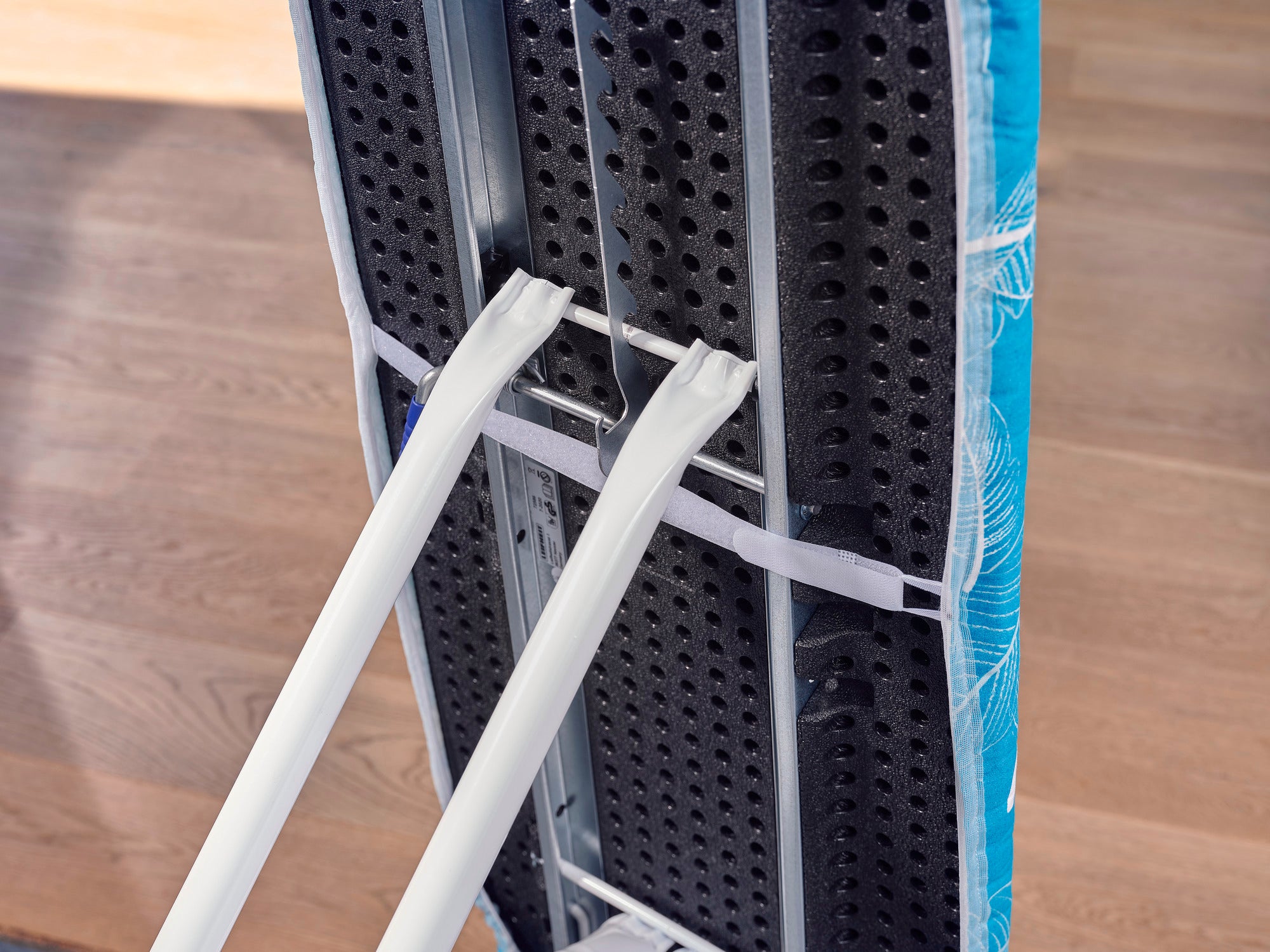 Table à repasser avec housse « Thermo Reflect M » en gros plan. La housse présente une surface réfléchissante qui rend le repassage plus efficace, sur un sol en bois.