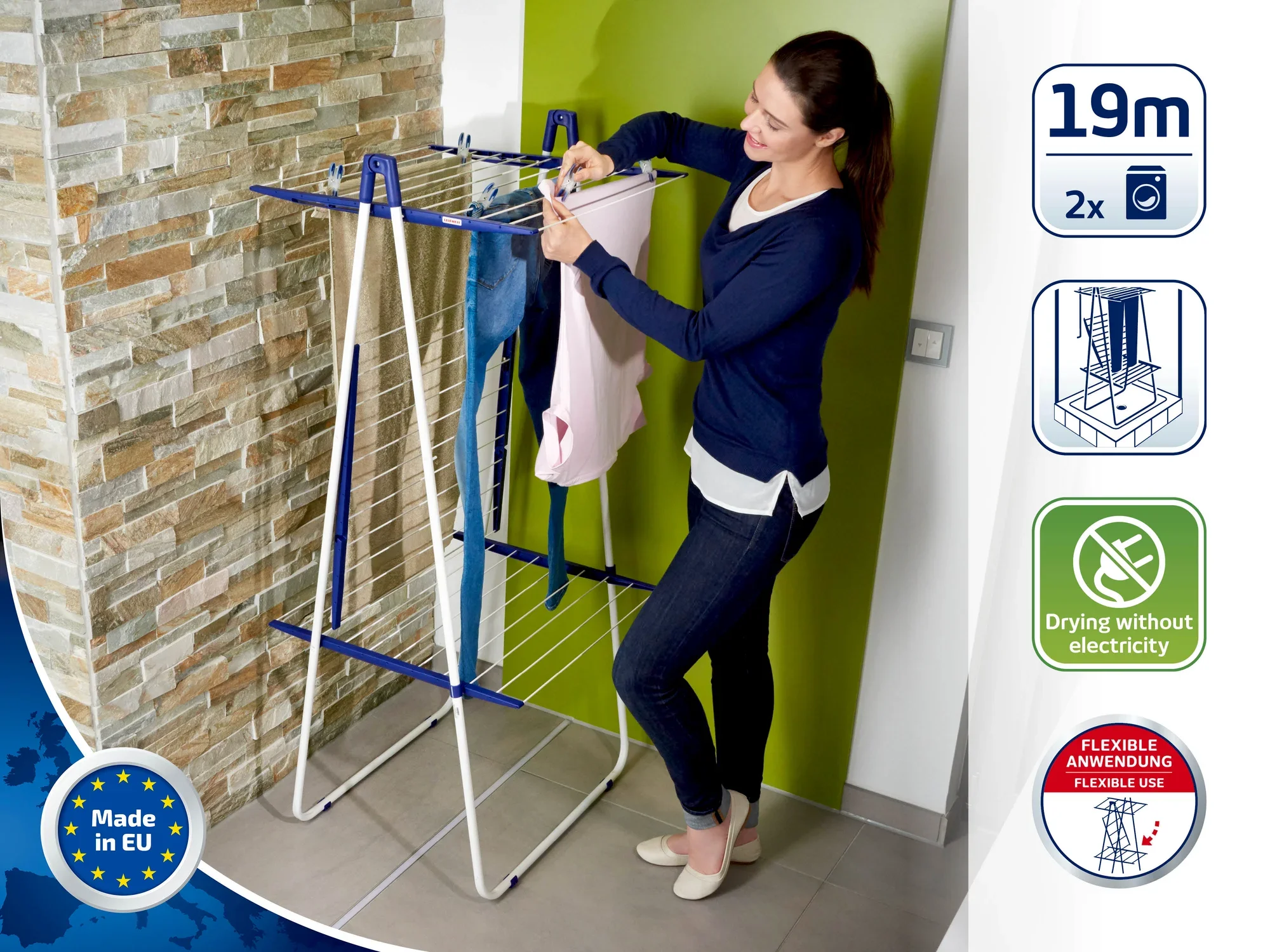 Een vrouw hangt kleding op aan een torendroger. De droger heeft ruimte voor 19 meter wasgoed en is ideaal voor gebruik binnenshuis. Gemaakt in de EU, zonder elektriciteitsverbruik.