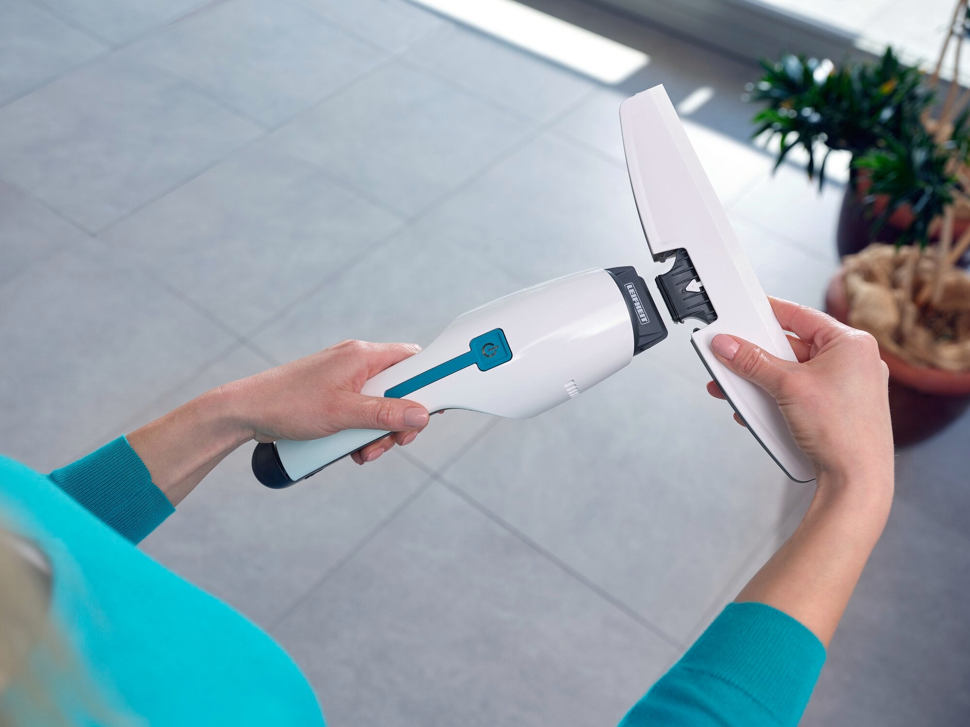 Eine Person hält den Nemo Fenstersauger, während sie ihn auf einer glatten Bodenfläche verwendet. Der Sauger ist weiß mit blauen Akzenten und wird in einem hellen Raum benutzt.