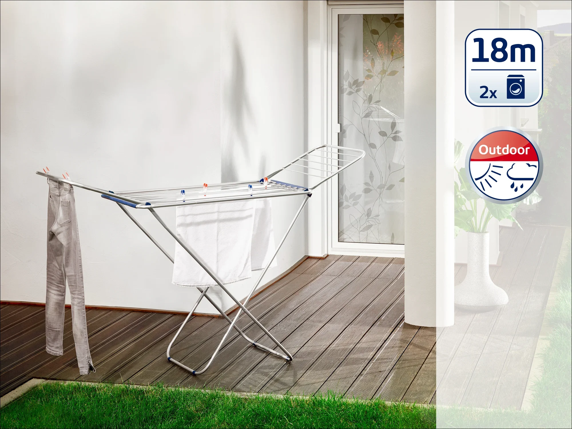 Een vrijstaande droogtrommel staat op een terras voor een glazen deur. Hij heeft een drooglengte van 18 meter en is geschikt voor buitengebruik. Er hangen twee handdoeken aan.