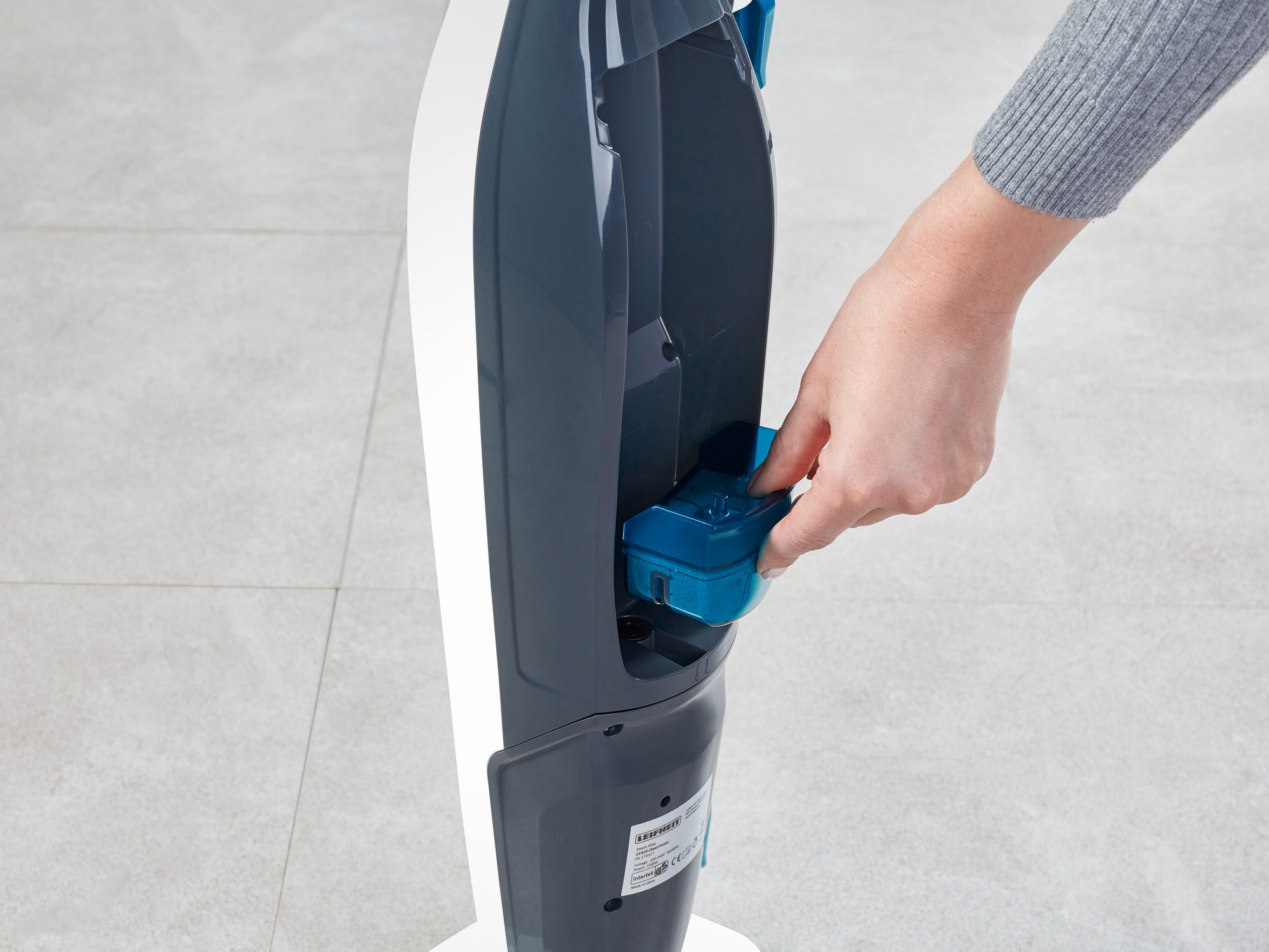 Eine Person legt eine blaue Kartusche in den Dampfreiniger Clean Tenso ein. Der Dampfreiniger steht auf einem hellen Boden und wird für die Reinigung vorbereitet.