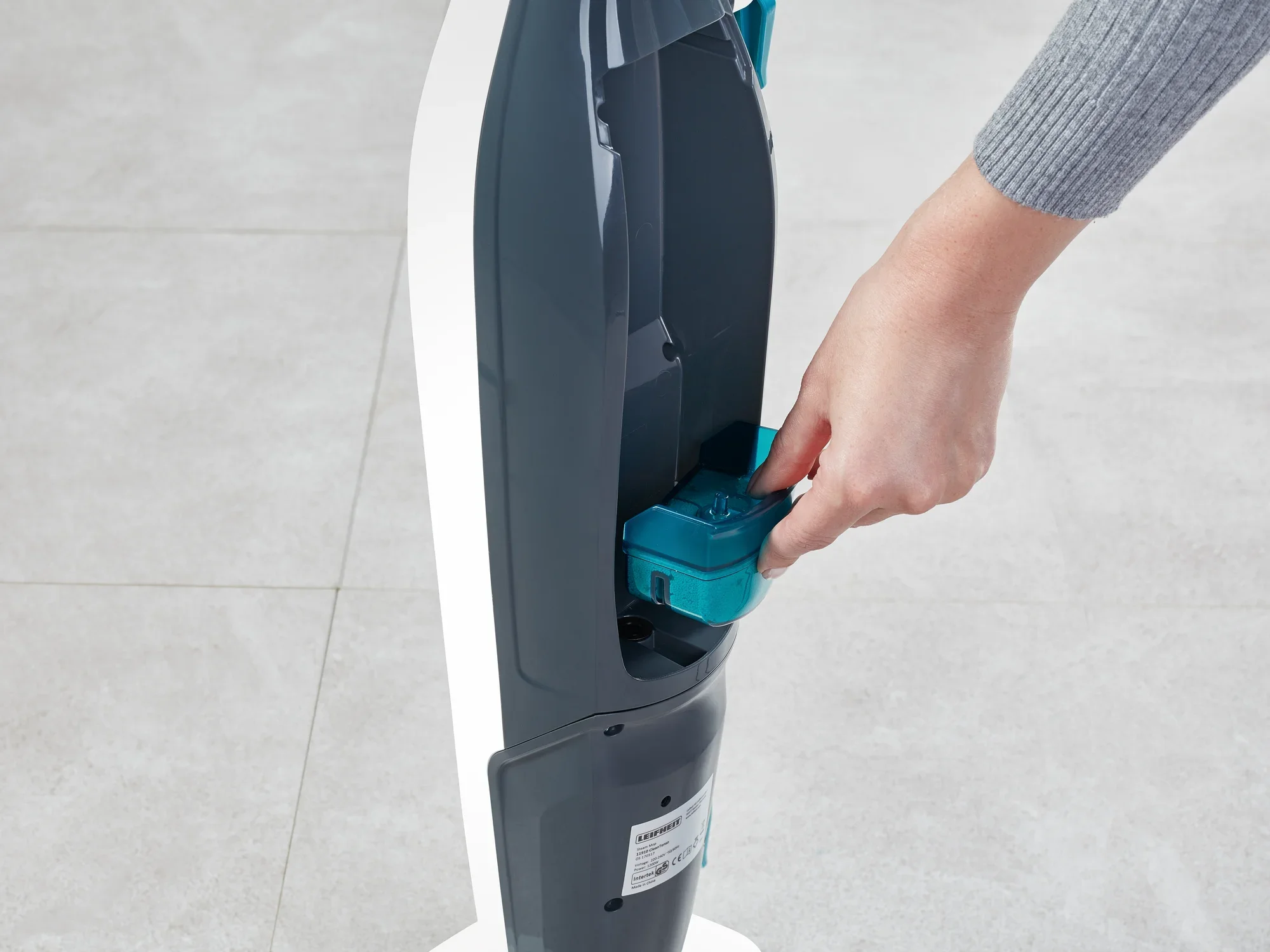 Eine Person legt eine blaue Kartusche in den Dampfreiniger Clean Tenso ein. Der Dampfreiniger steht auf einem hellen Boden und wird für die Reinigung vorbereitet.