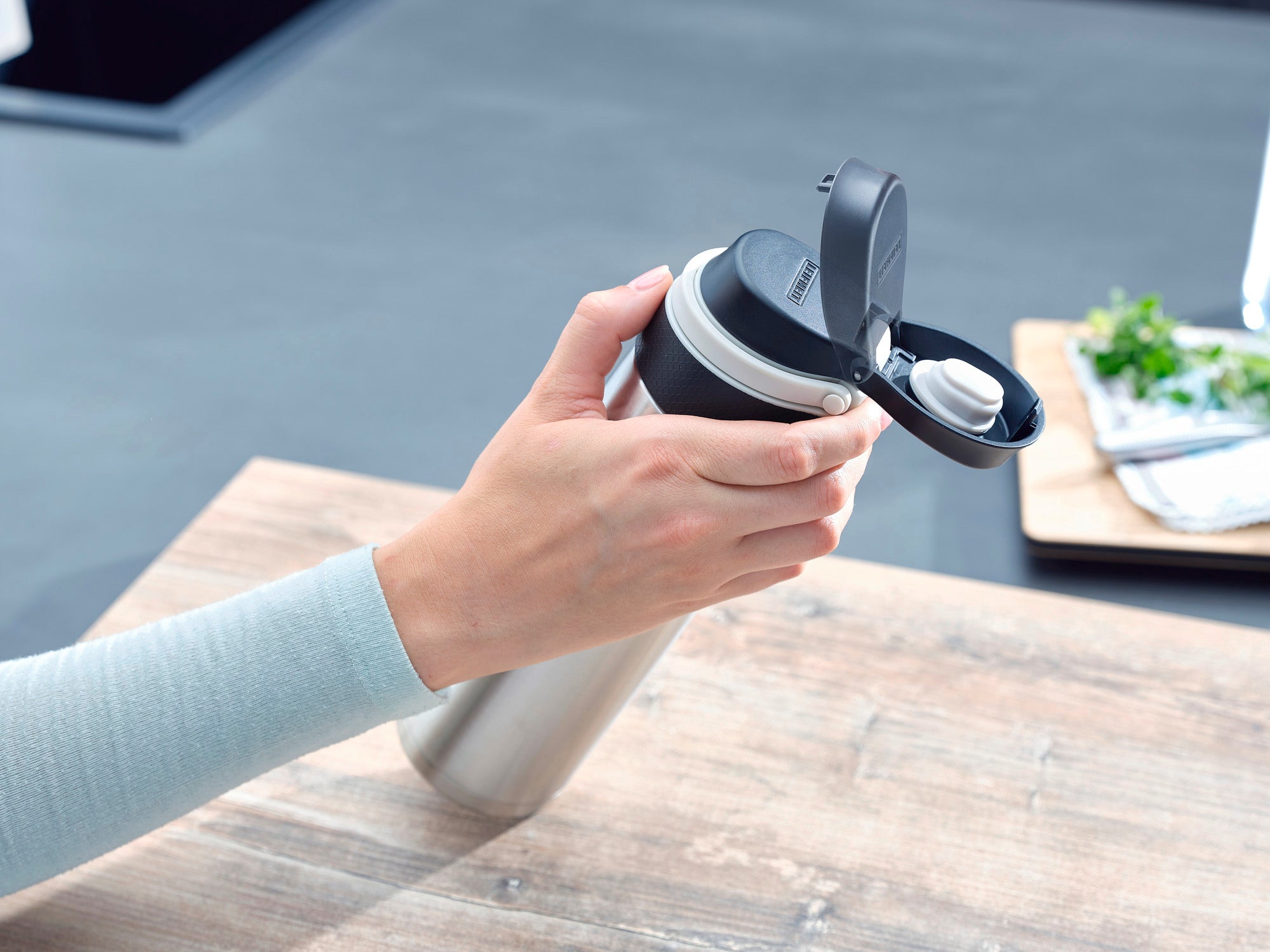 Isolierbecher Flip 600ml in Silber wird von einer Hand gehalten. Der Becher hat einen praktischen Klappdeckel, ideal für unterwegs. Perfekt für heiße und kalte Getränke.