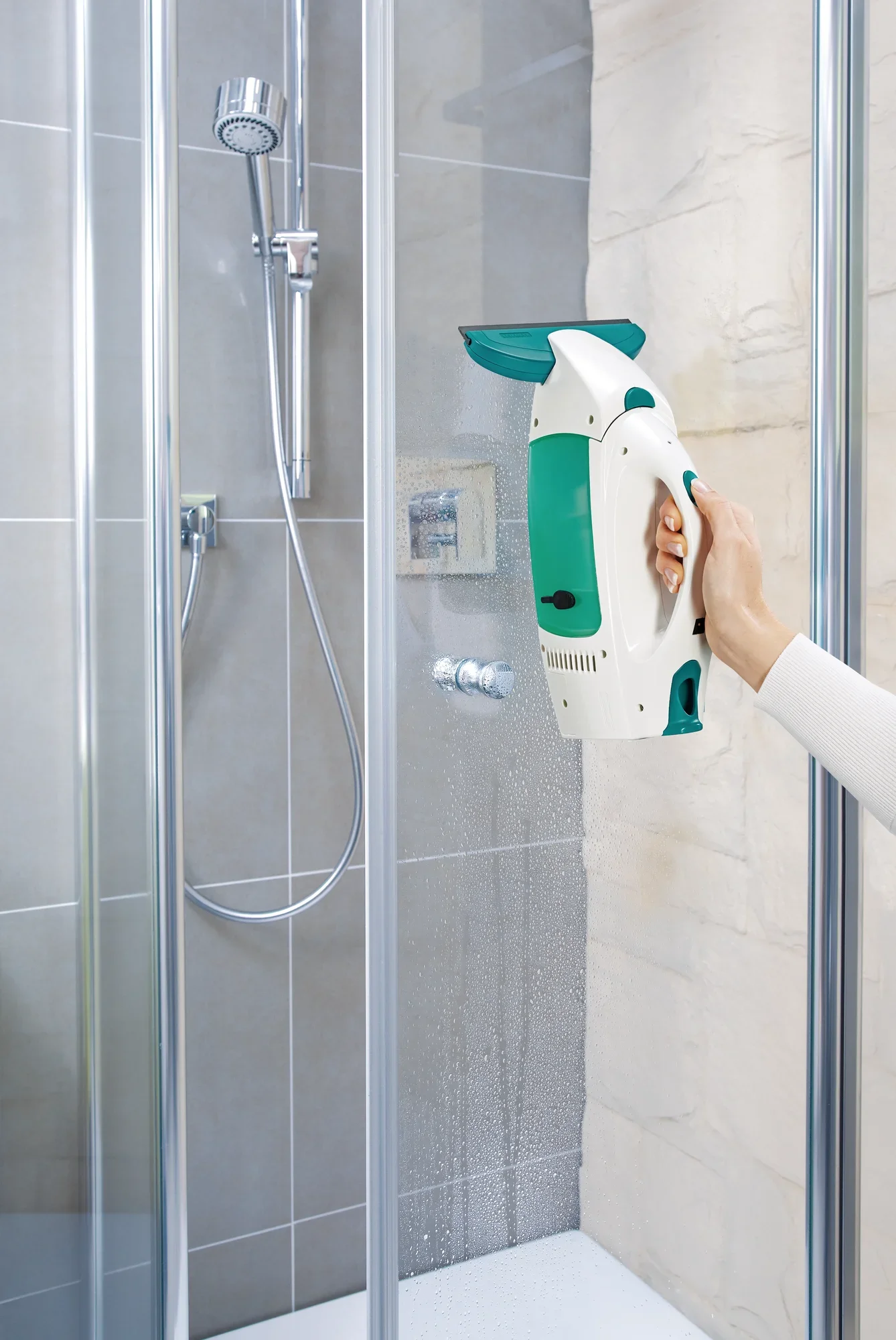 Ein Fenstersauger Dry and Clean mit kleiner Düse wird in einer Dusche verwendet. Eine Hand hält das Gerät, während es Wasser von der Duschwand absaugt. Ideal für streifenfreie Sauberkeit.