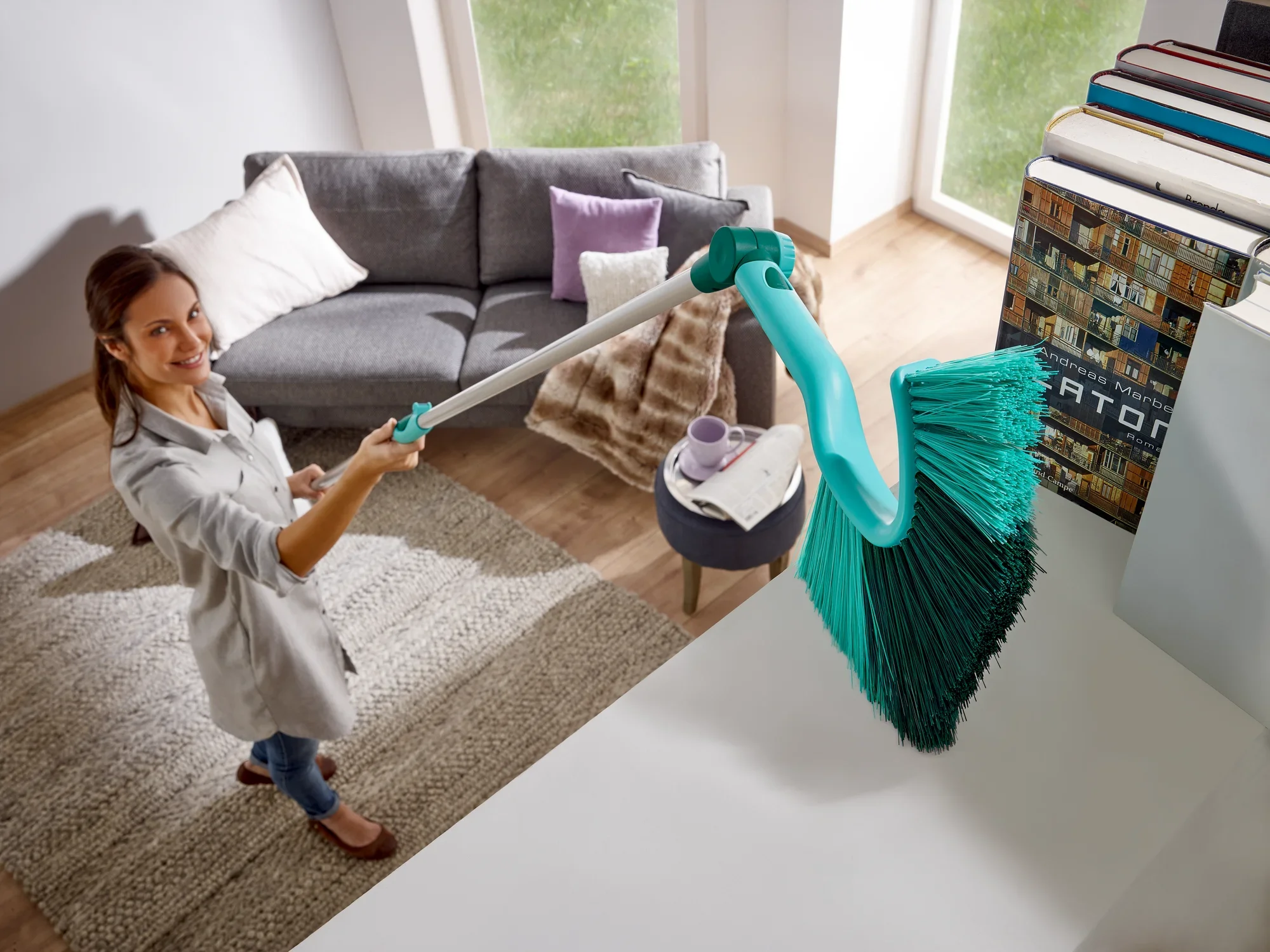 Een vrouw gebruikt de SUPERDUSTER stofbezem met telescopische steel om hoge oppervlakken in een moderne woonkamer schoon te maken. De bezem heeft lange, dichte haren.
