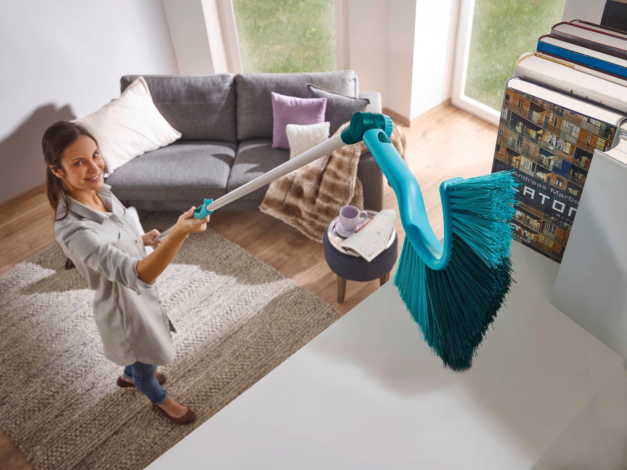 Une femme utilise le balai à poussière avec manche télescopique pour nettoyer les surfaces en hauteur dans un salon moderne. Le balai a des poils longs et denses.