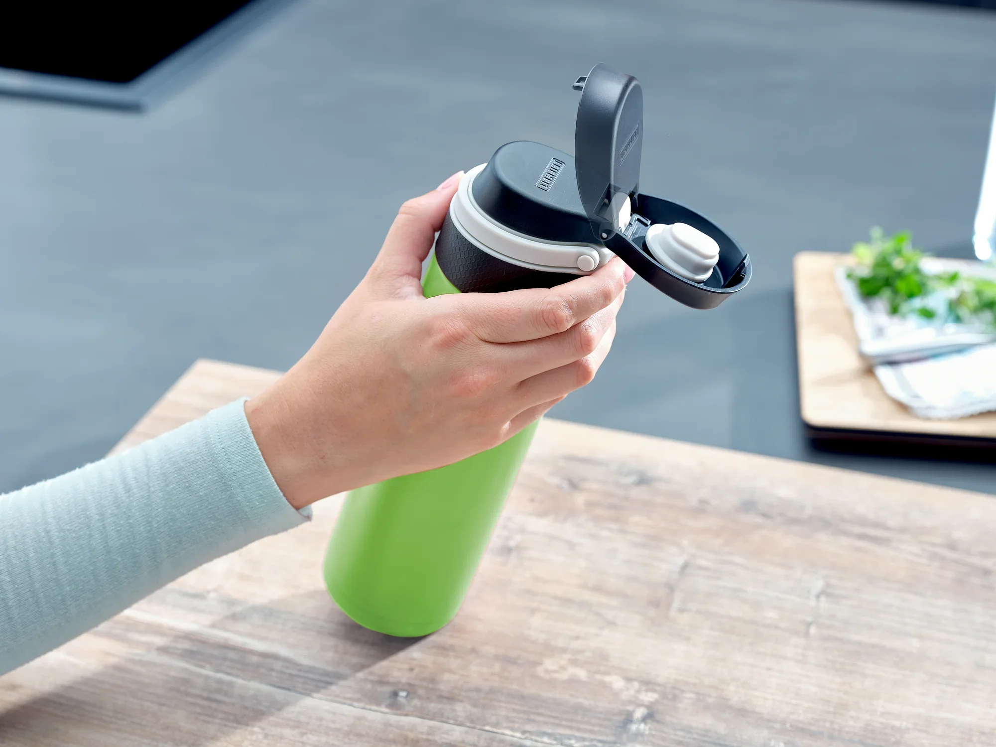 Izolowany kubek Flip 600 ml w kolorze kiwi jest używany na stole. Ręka otwiera pokrywkę, aby pokazać praktyczne zamknięcie. Idealny w podróży.
