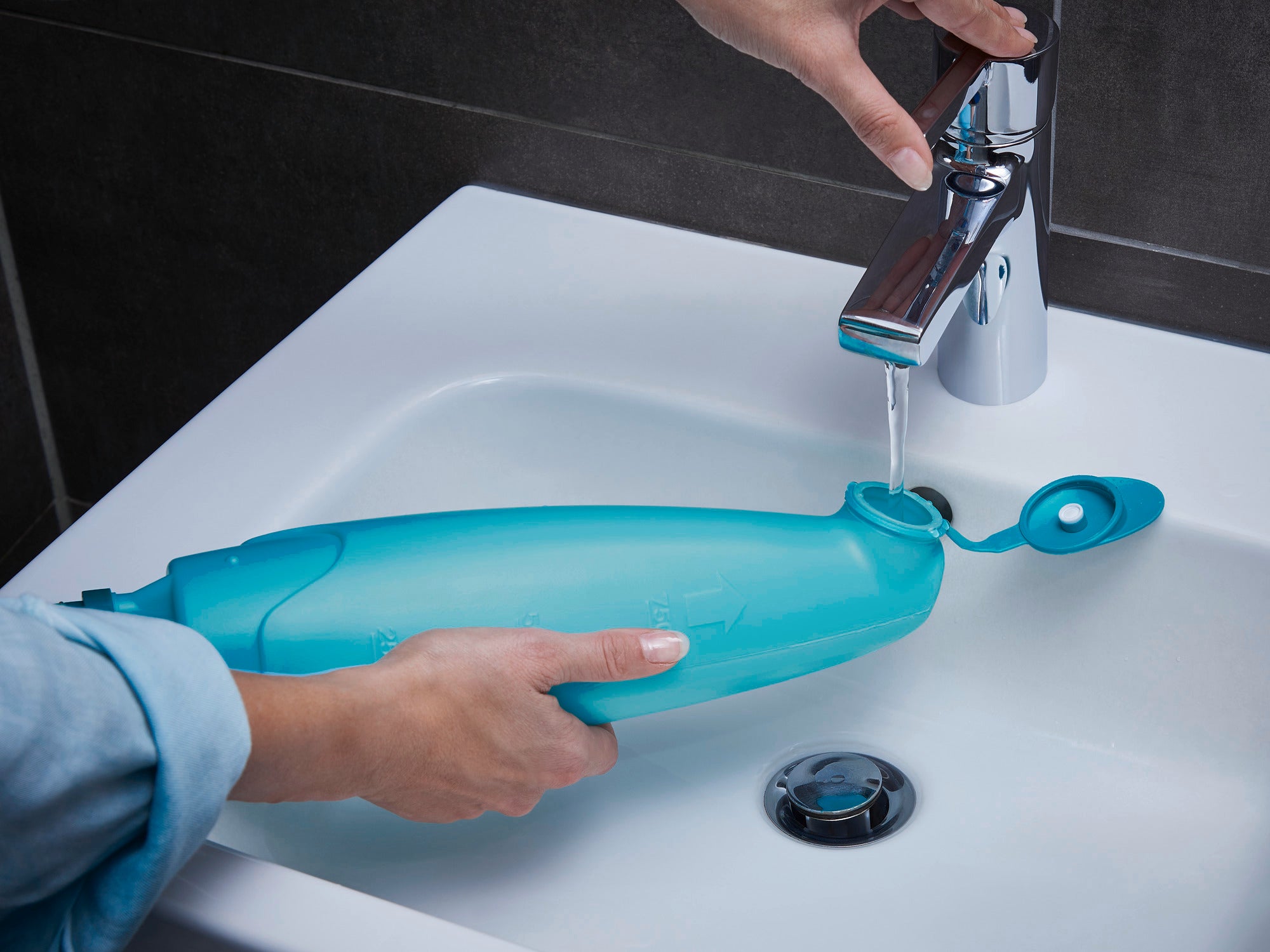 Eine Person füllt den Wassertank des Sprühwischers Pico Spray an einem Waschbecken auf. Der blaue Tank hat einen offenen Deckel und wird unter fließendem Wasser gehalten.