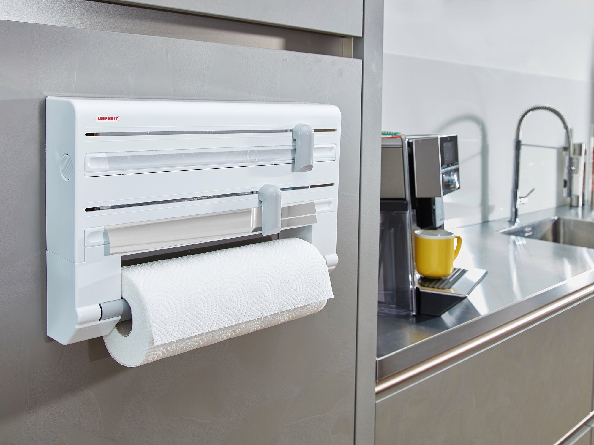 Support mural pour rouleaux Parat installé dans une cuisine moderne. Le support est blanc et peut accueillir un rouleau de papier essuie-tout. Une machine à café et un évier sont visibles à l'arrière-plan.