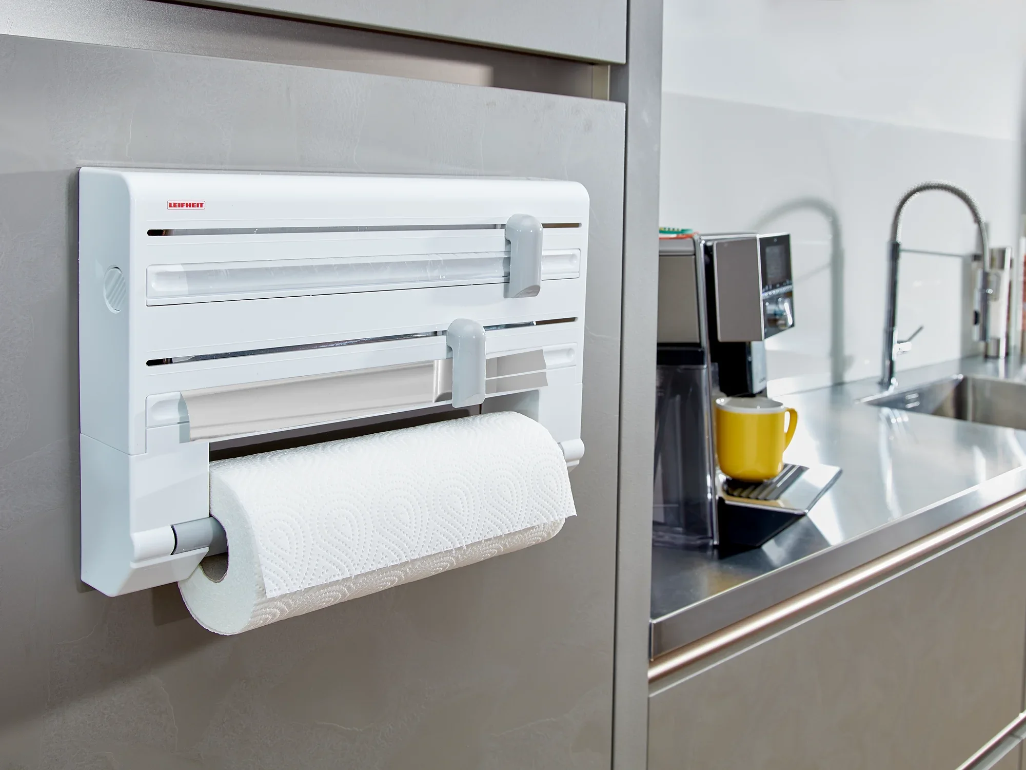 Support mural pour rouleaux Parat installé dans une cuisine moderne. Le support est blanc et peut accueillir un rouleau de papier essuie-tout. Une machine à café et un évier sont visibles à l'arrière-plan.