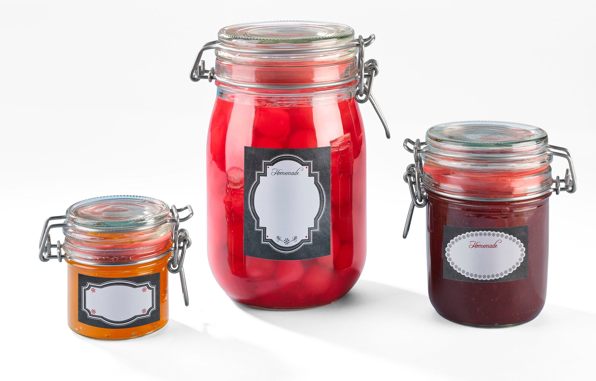 Trois bocaux avec des étiquettes décoratives noires. Le plus grand bocal contient des boules rouges, le bocal du milieu contient un liquide rouge et le plus petit contient un liquide orange.