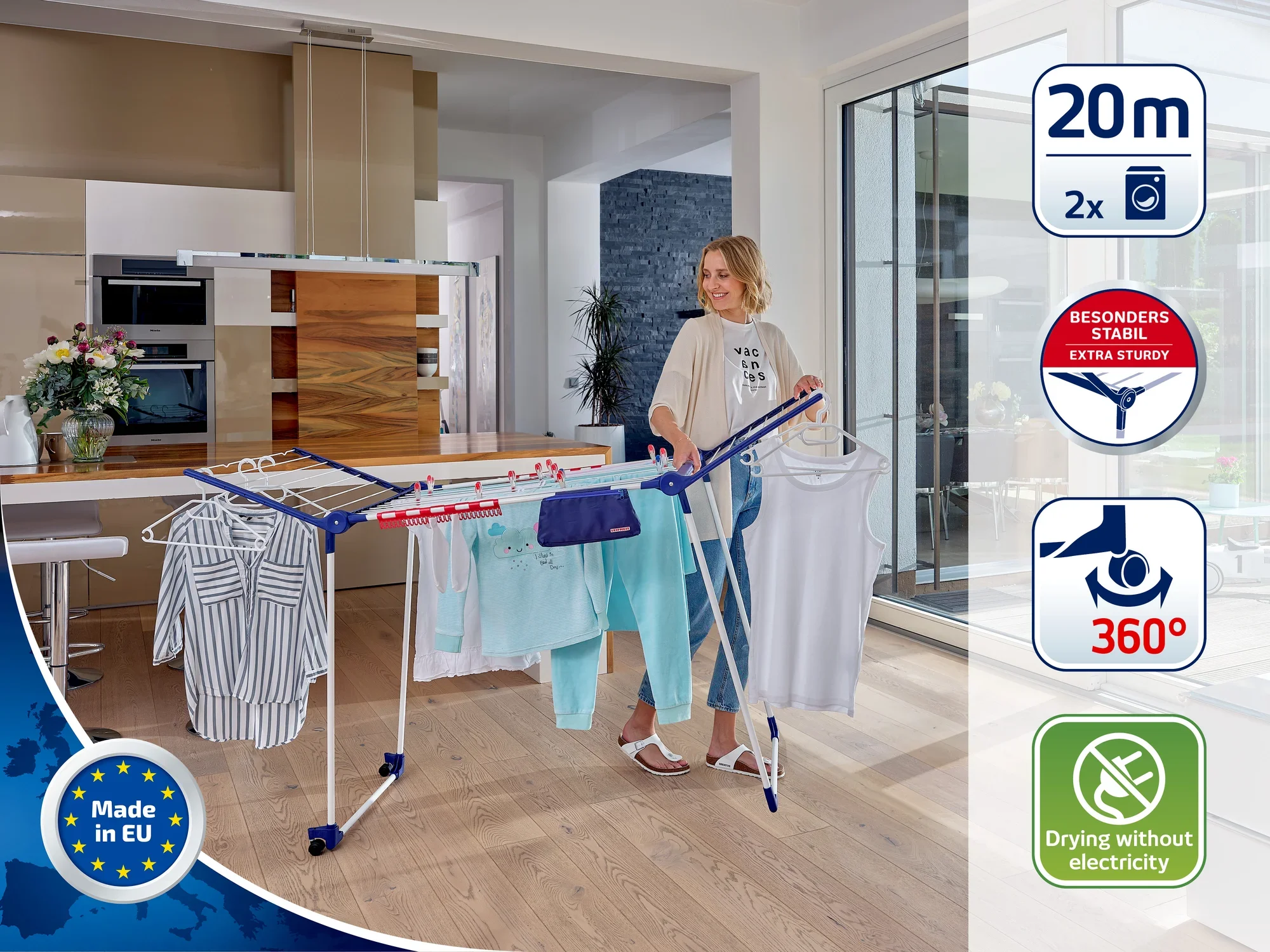 Een vrouw staat in een moderne woonkamer en gebruikt een vrijstaande wasdroger om kleding te drogen. De droger heeft een drooglengte van 20 meter en is bijzonder stabiel. Ideaal voor milieuvriendelijk drogen zonder elektriciteit.