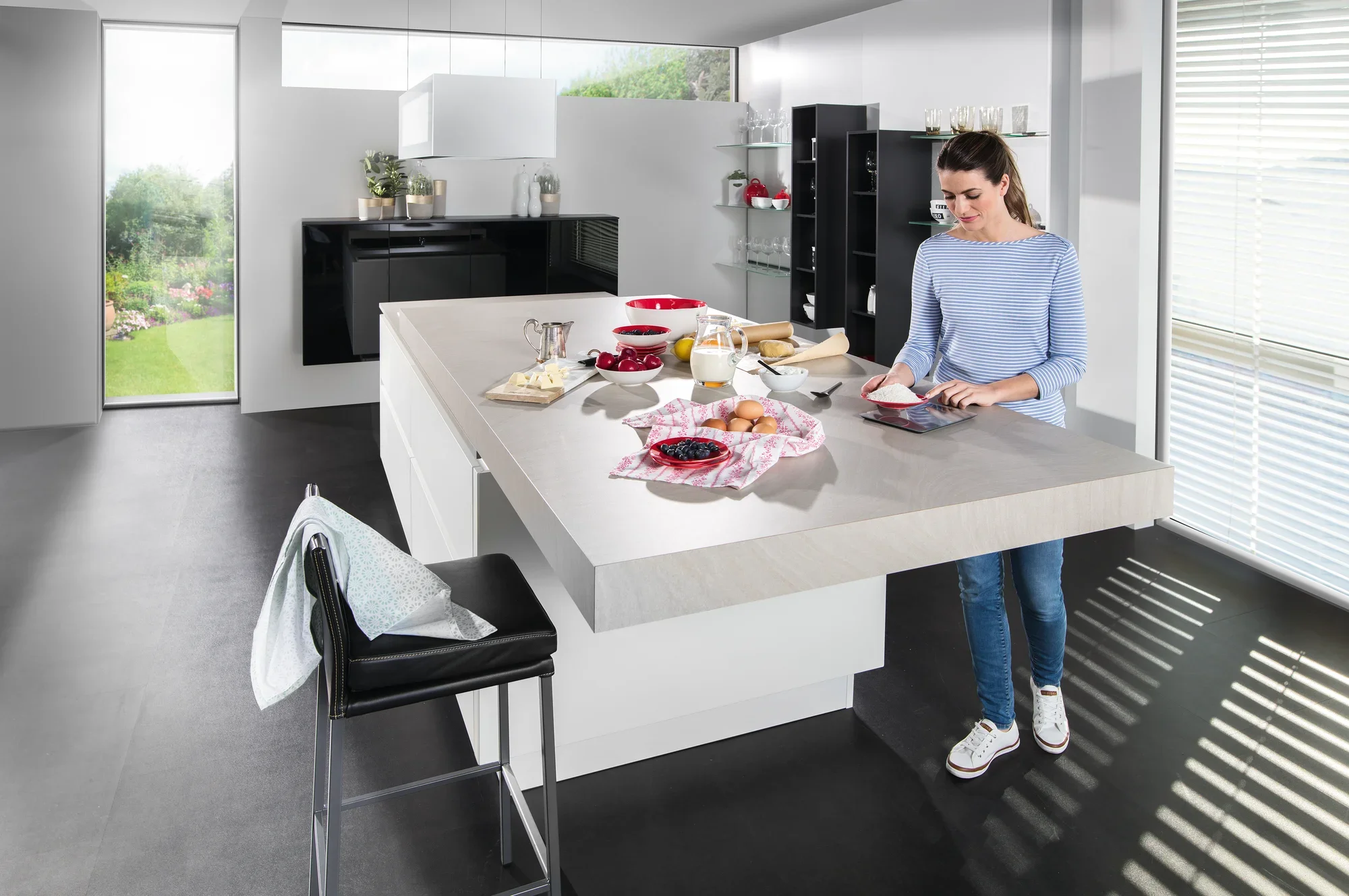 Een vrouw in een moderne keuken gebruikt de Page Comfort 300 Slim digitale keukenweegschaal. Op het werkblad staan ingrediënten en een schaaltje bessen.
