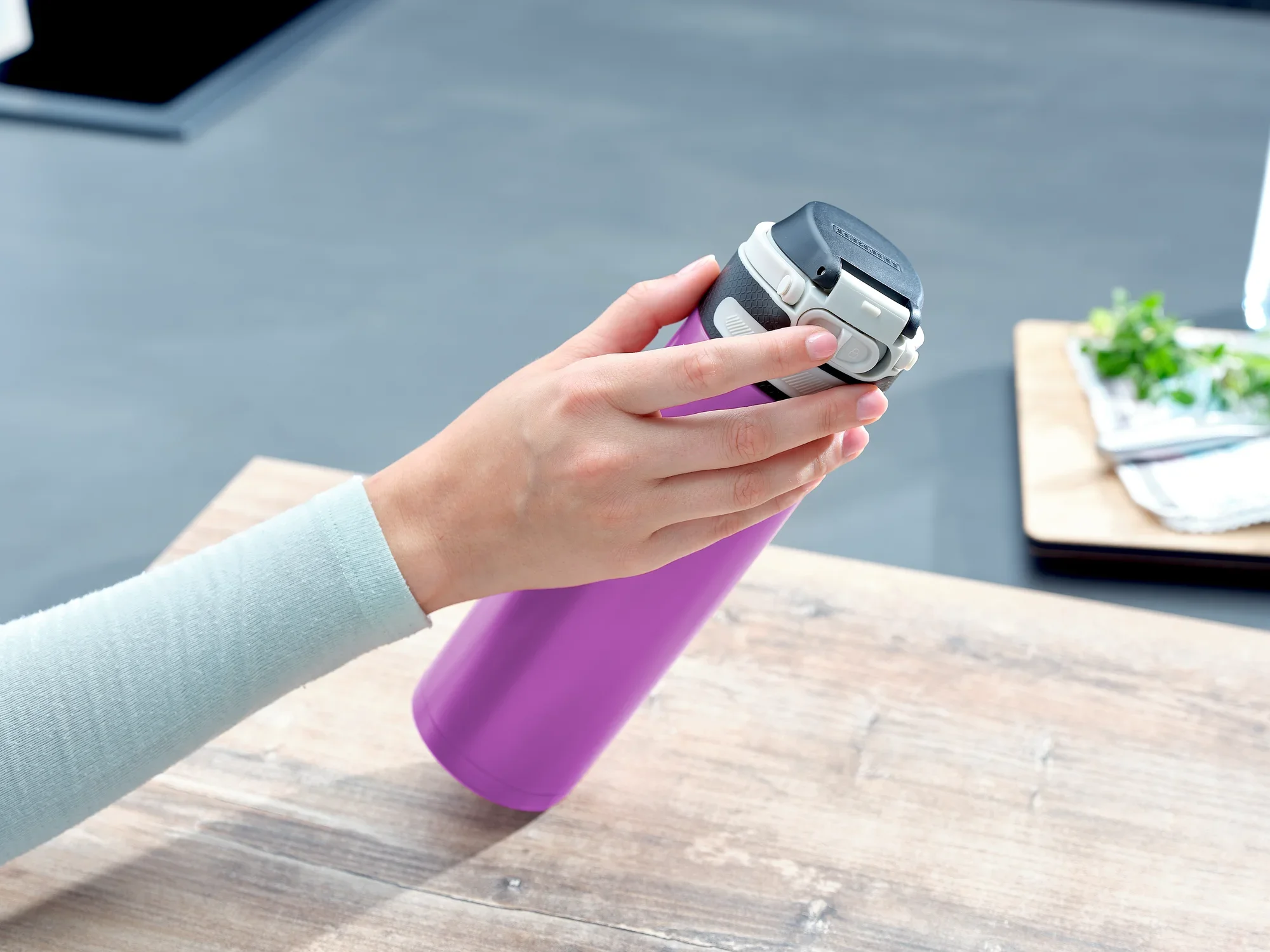 Flip 600ml vacuüm mok in paars op een tafel. Een hand opent het deksel van de mok. Op de achtergrond zijn keukengerei en verse kruiden te zien.