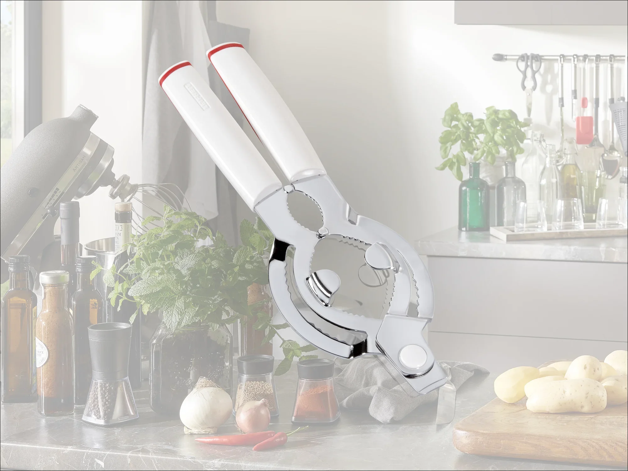 Ein hochwertiger Flaschenöffner mit ergonomischen weißen Griffen liegt auf einer modernen Küchenarbeitsplatte. Im Hintergrund sind Kräuter, Gewürze und Küchenutensilien zu sehen.