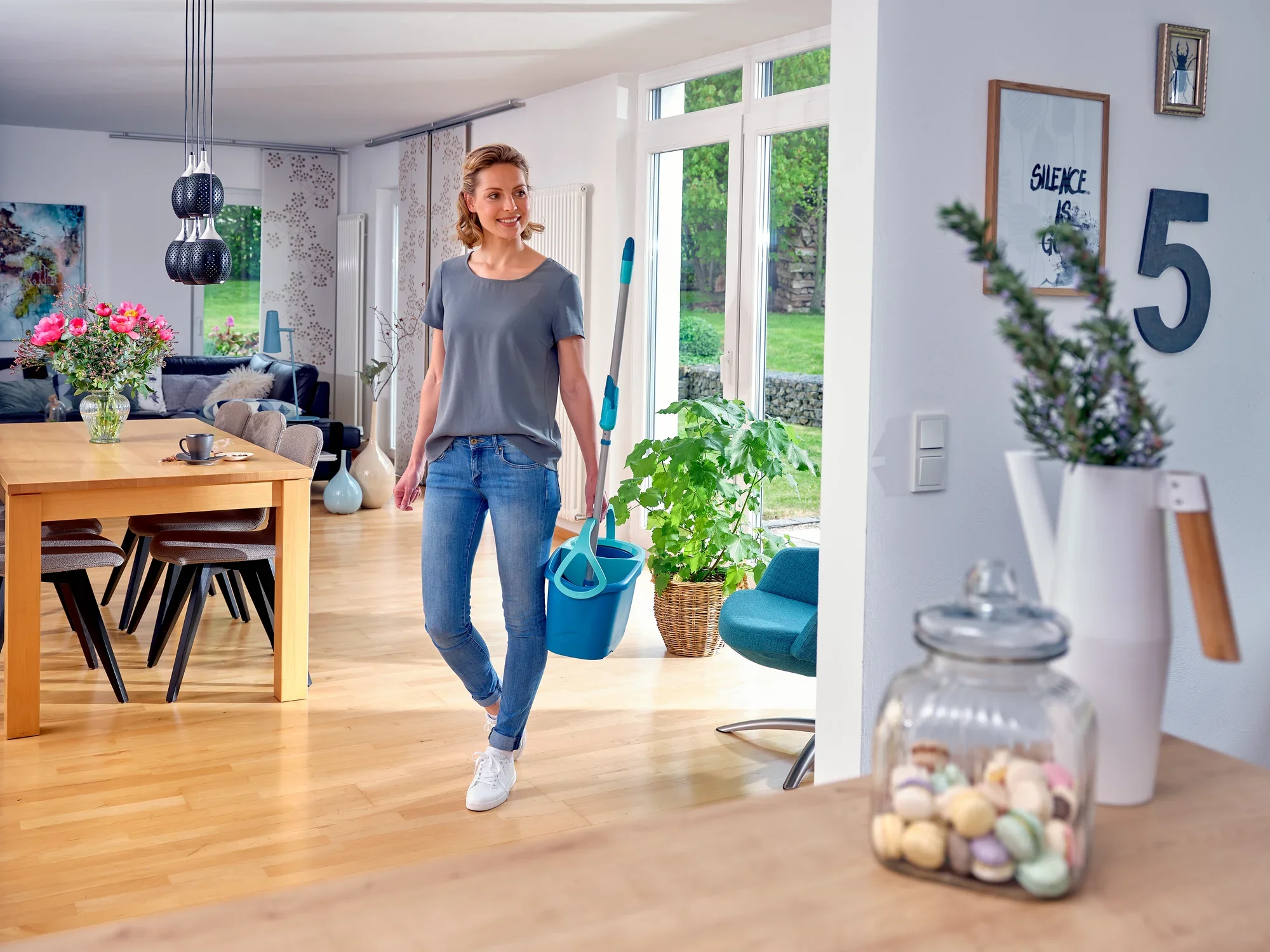 Una donna attraversa un soggiorno moderno con in mano il set CLEAN TWIST Mop. La stanza è luminosa e accogliente, con grandi finestre e arredata con stile. Piante e decorazioni conferiscono alla stanza un'atmosfera accogliente.