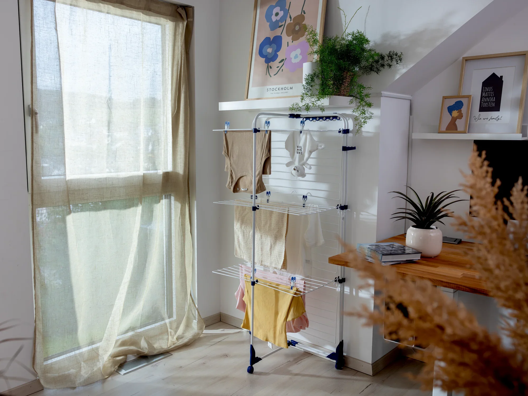 Een torendroger, de Classic Tower 340, staat in een lichte kamer naast een raam. Hij is volgeladen met wasgoed en omringd door planten en decoraties, wat een gezellige sfeer creëert.